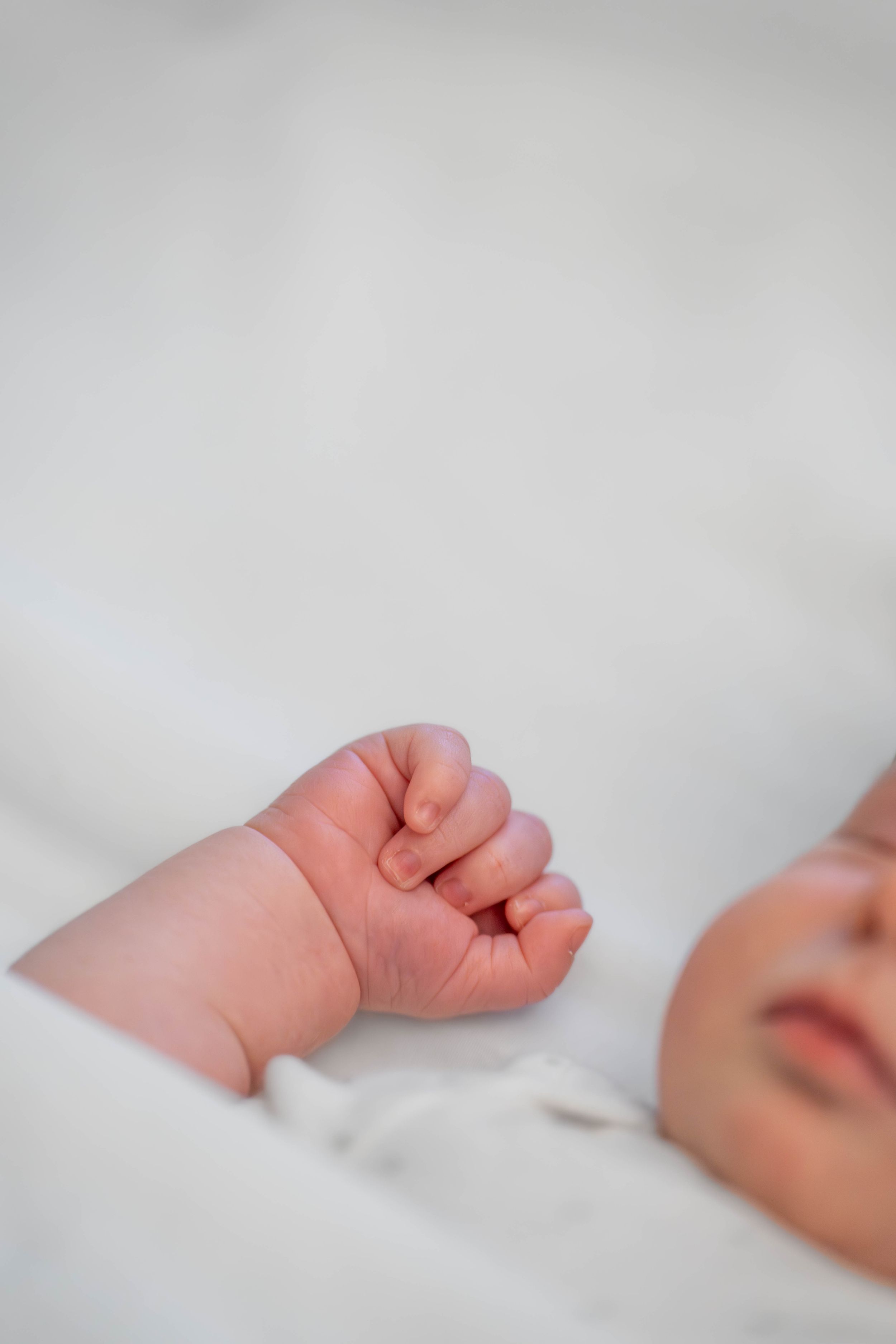 Close-up of tiny curled baby fingers against white fabric in soft lighting. Quad Cities Newborn Photography