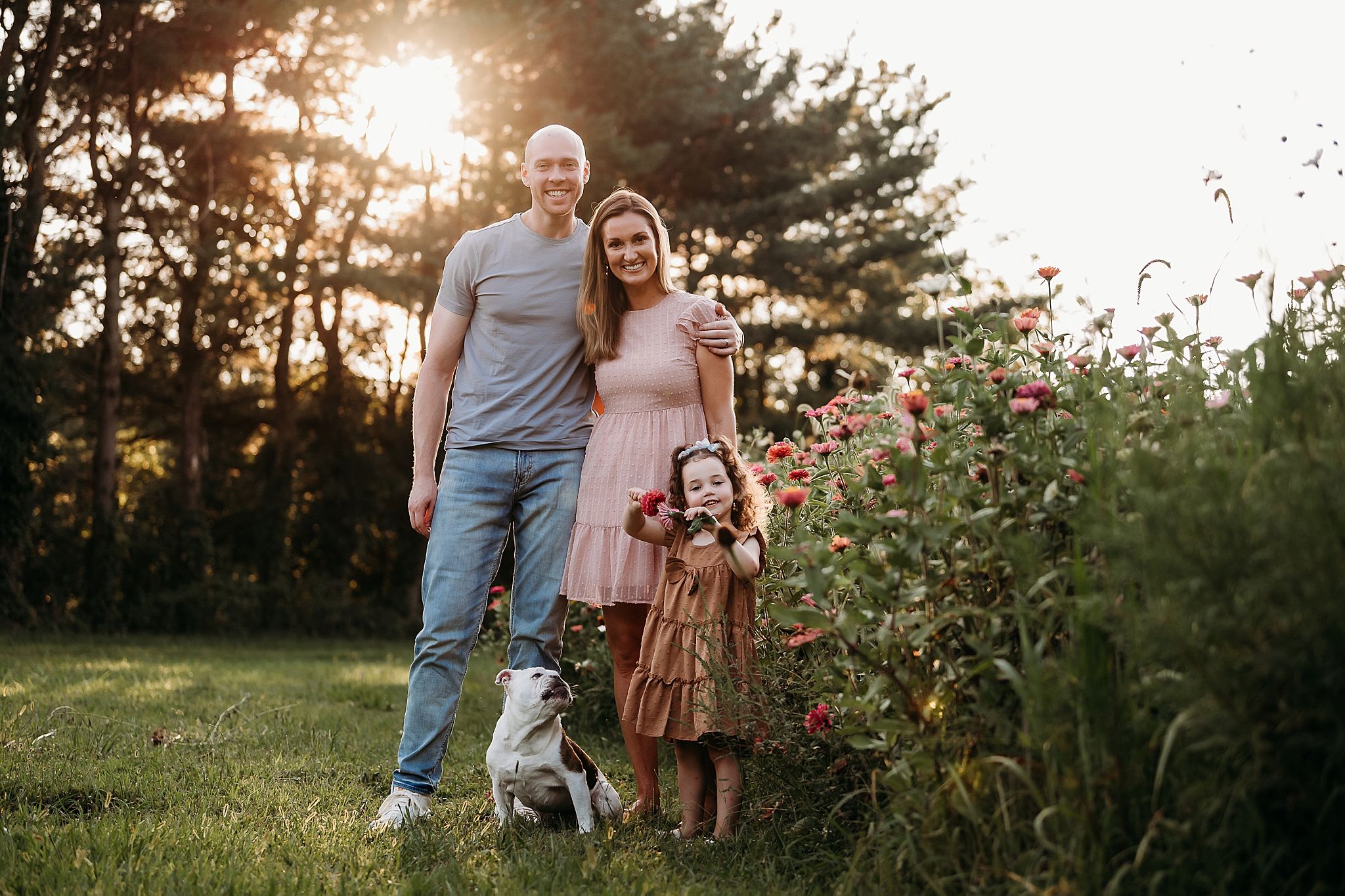 A golden sunset illuminates a garden scene with people sharing a joyful moment together near flowering plants.