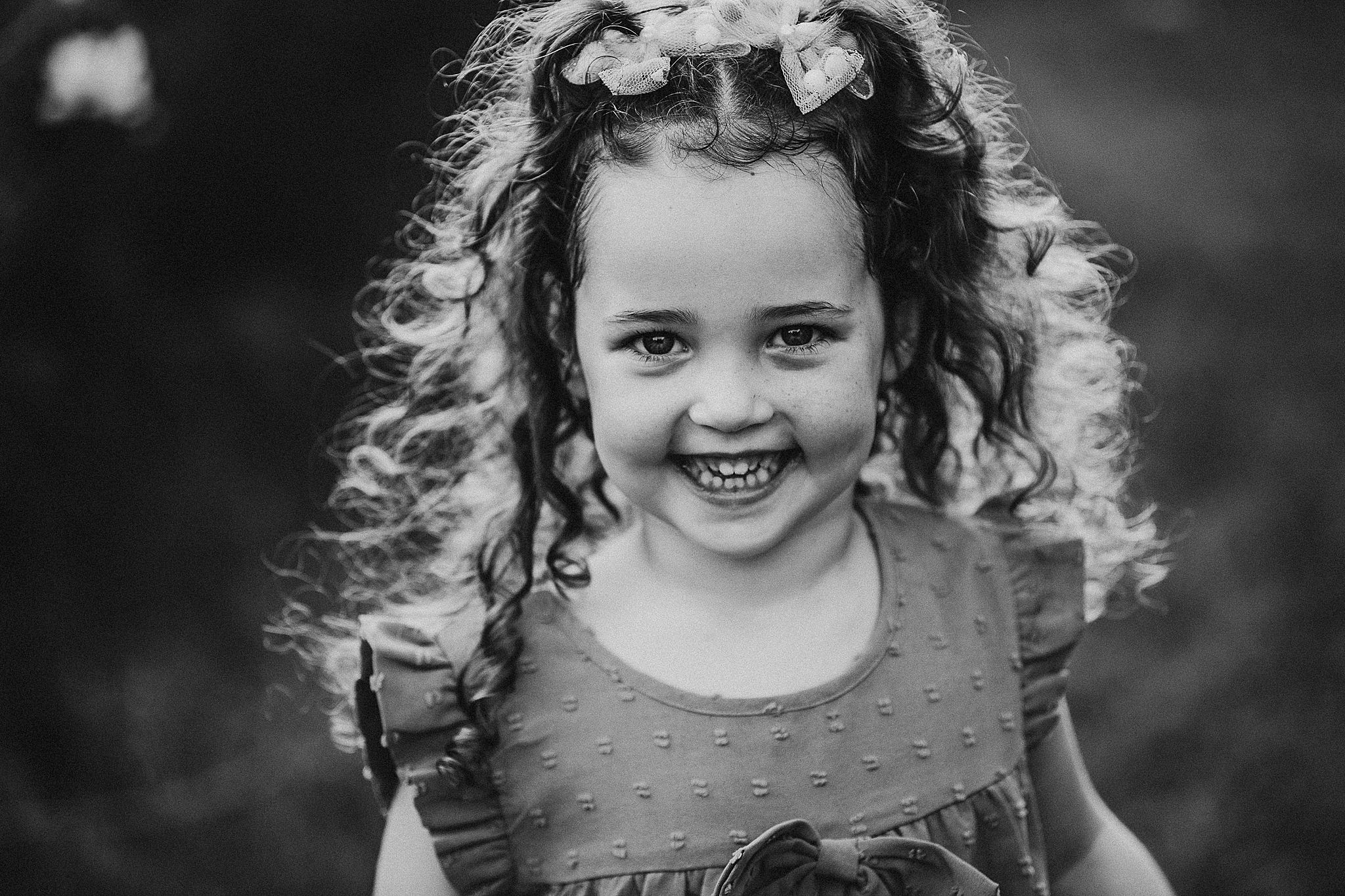 Black and white portrait of a child with curly hair smiling brightly in natural light.