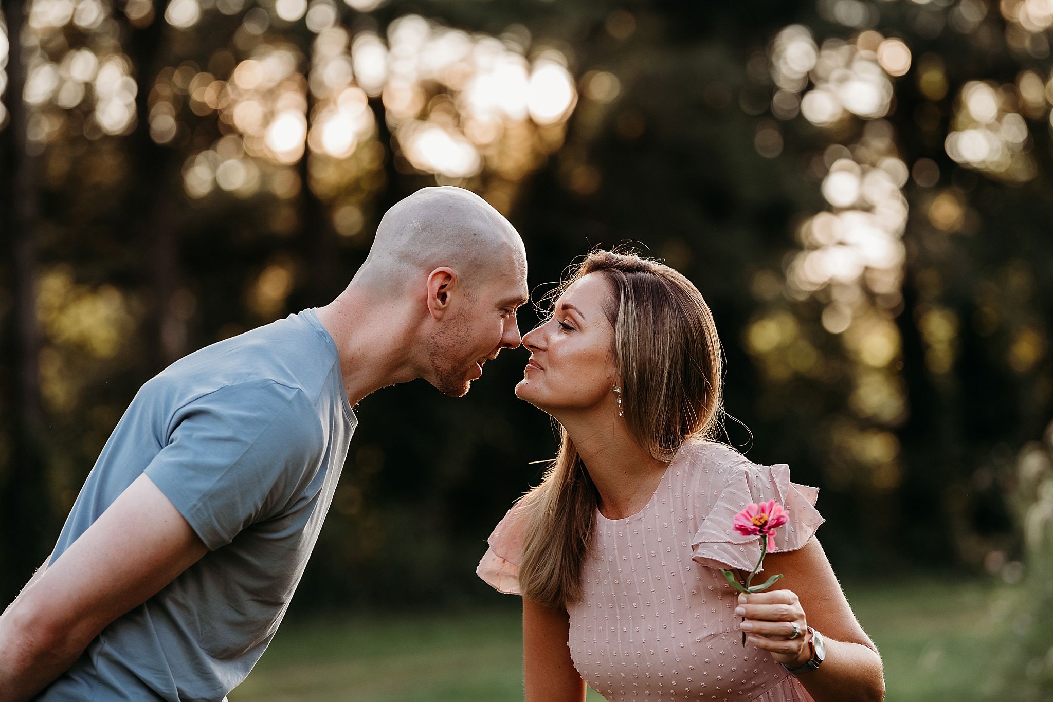 A romantic couple shares an intimate kiss in a sunlit forest setting as the golden light filters through the trees.