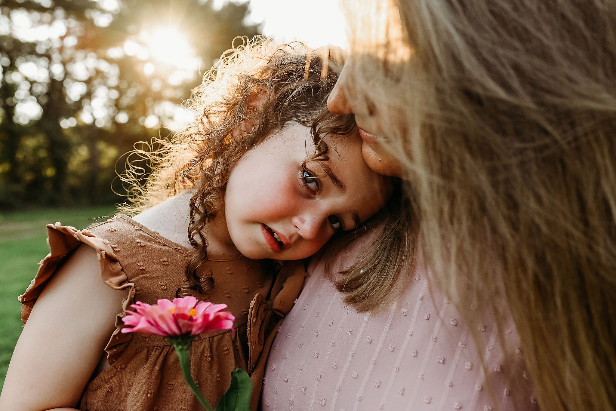 A tender moment captured at sunset with curly hair and a pink flower against a sunny outdoor background.