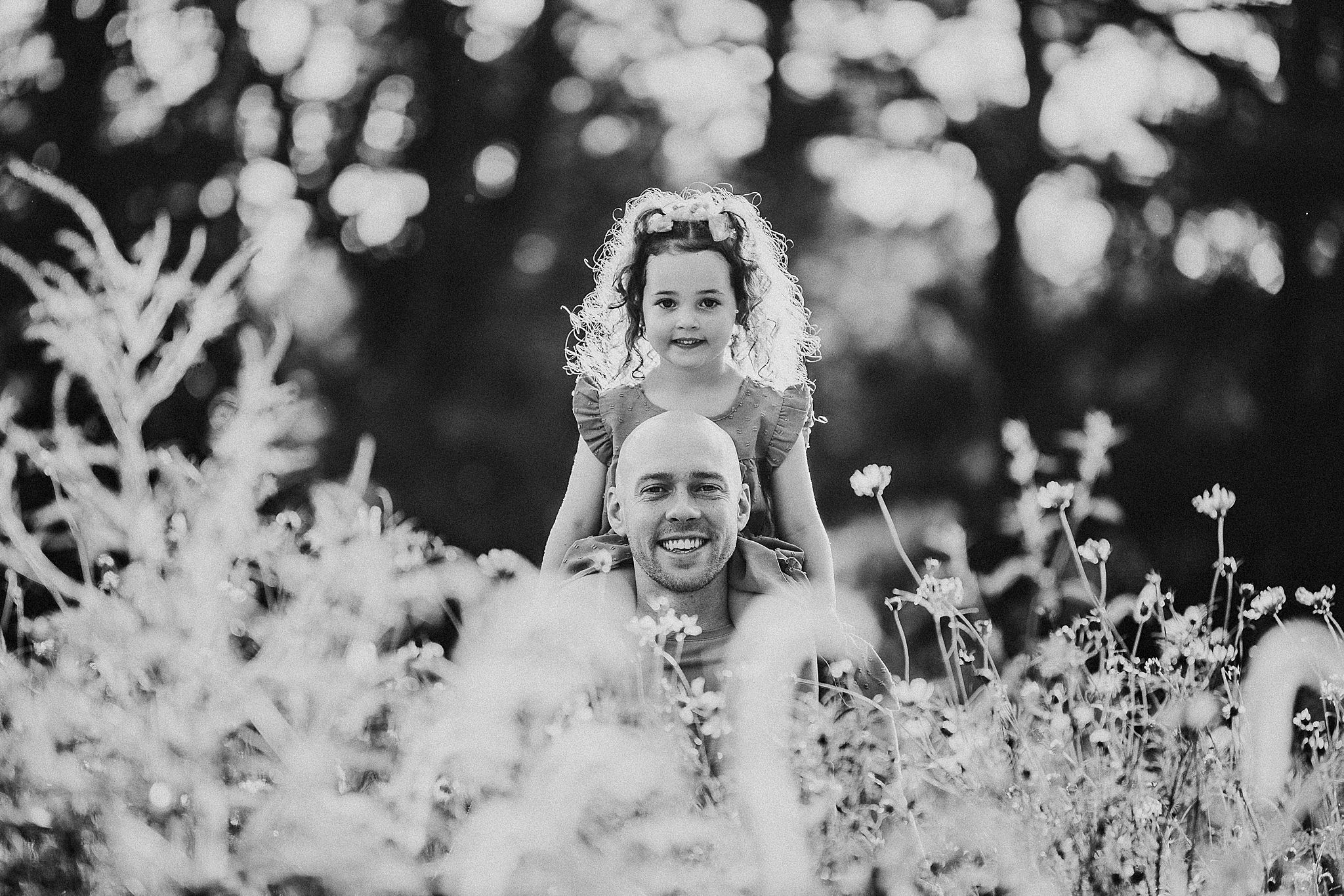 Black and white photo of a parent and child spending time together outdoors among wildflowers on a sunny day.