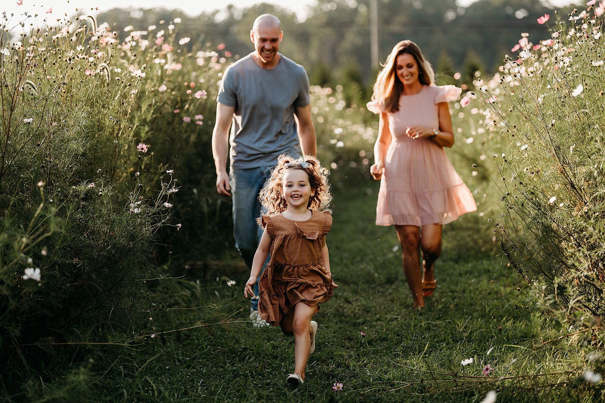 A happy family walks through a wildflower meadow at sunset with tall white daisies blooming around them.
