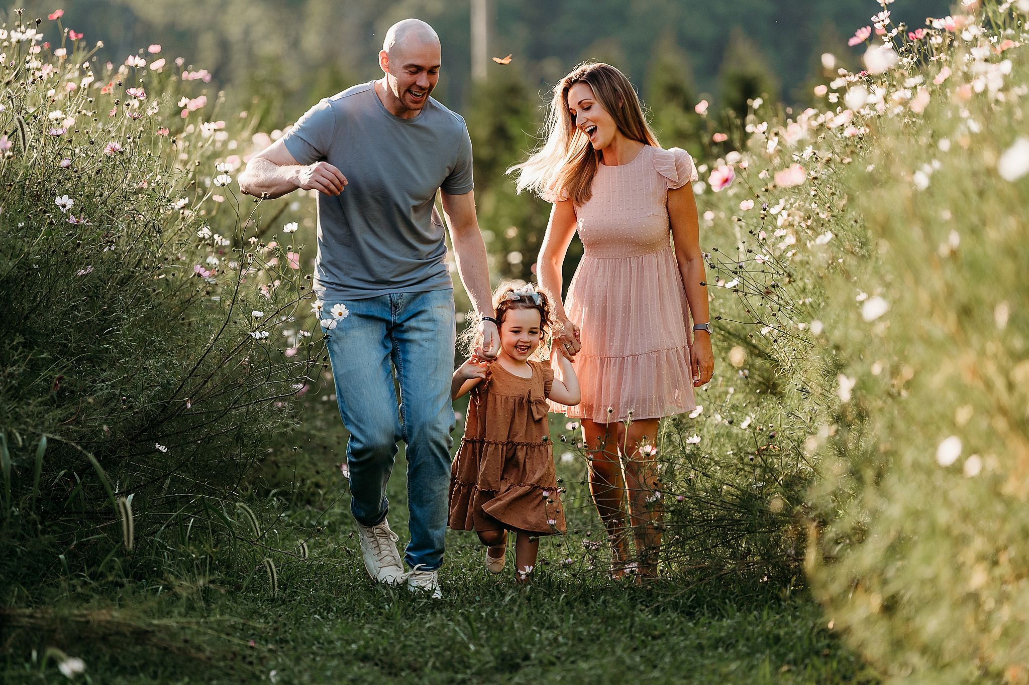 Adults and children walk together through a serene meadow filled with delicate white wildflowers at sunset.