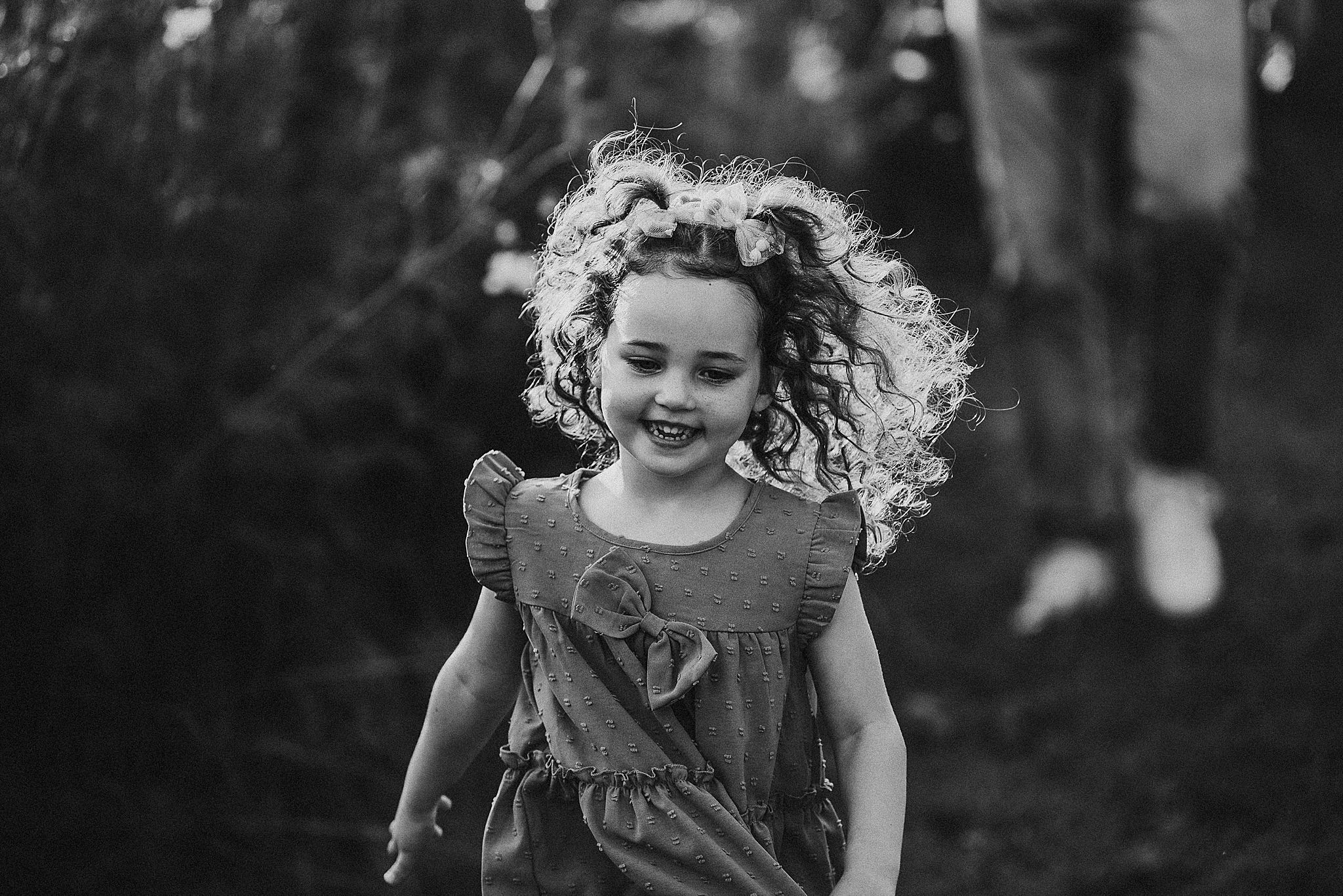 A young child runs with curly hair flying in the breeze wearing a ruffled dress in black and white.