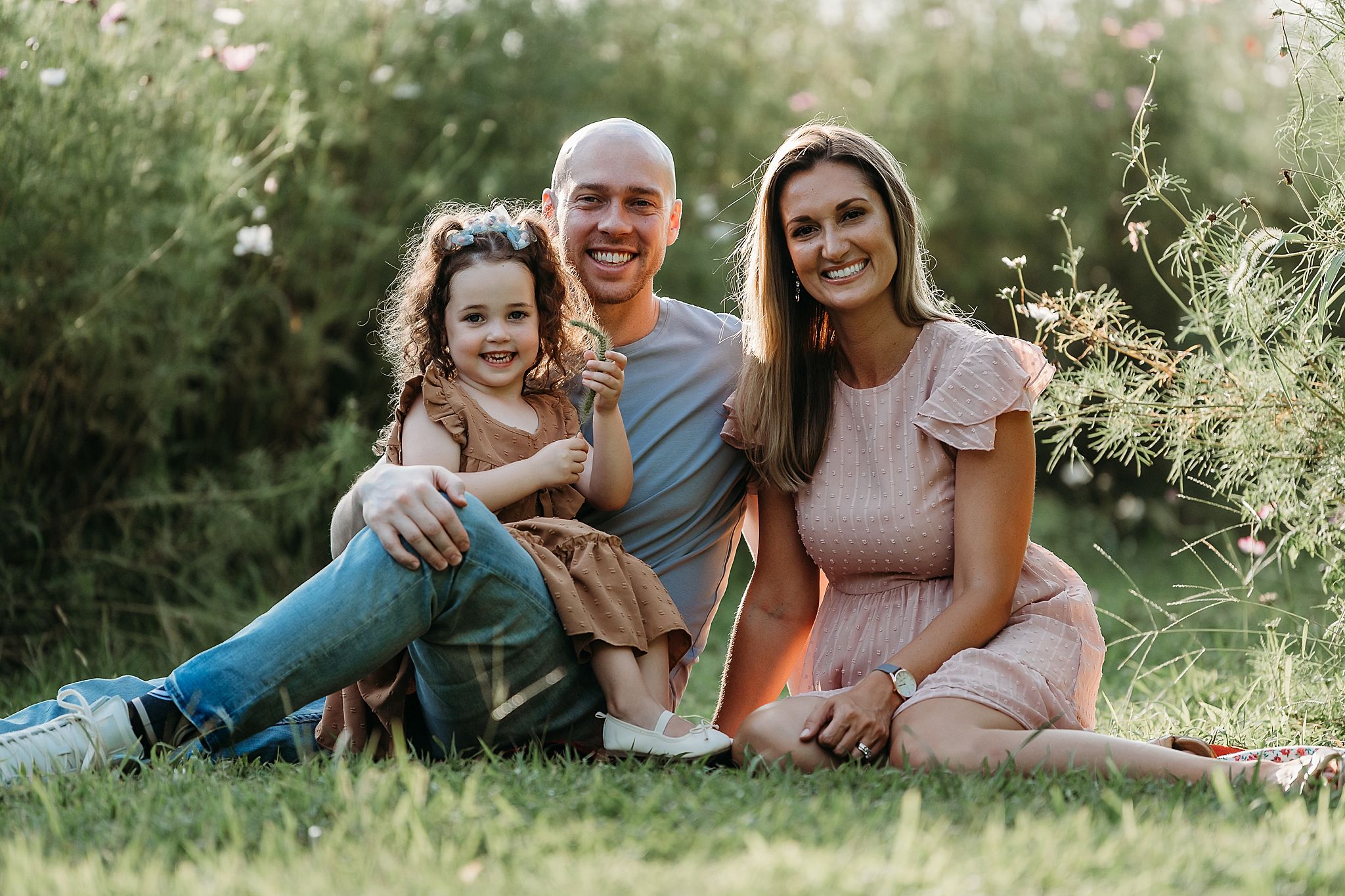 People sitting together on grass in a sunny garden during golden hour photoshoot.