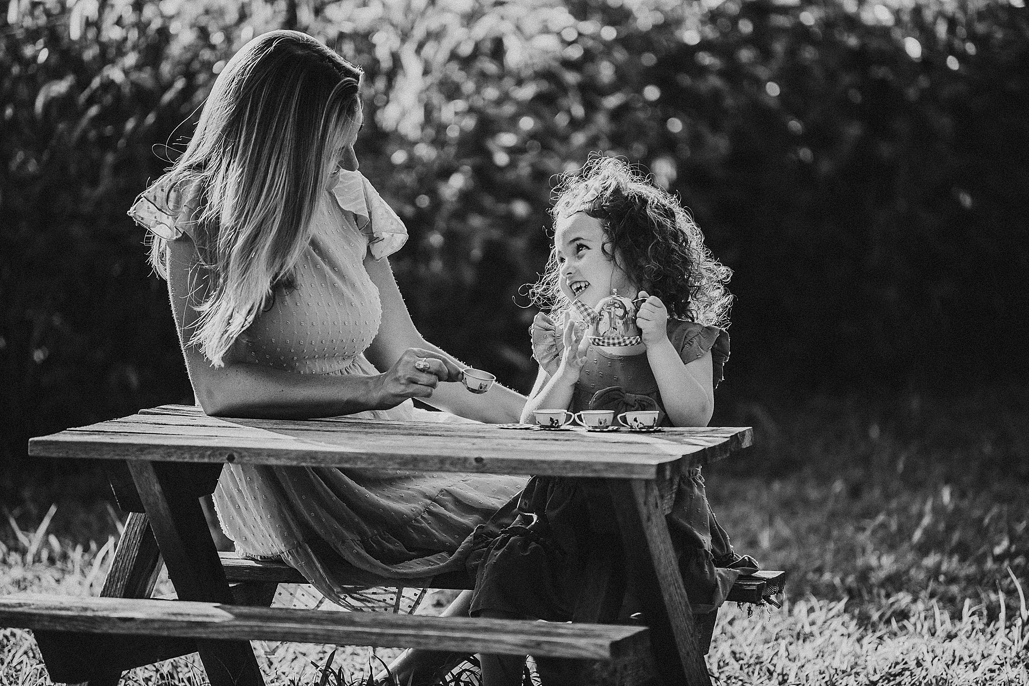 Black and white photo of adult and child sharing conversation while sitting at outdoor picnic table in nature setting.