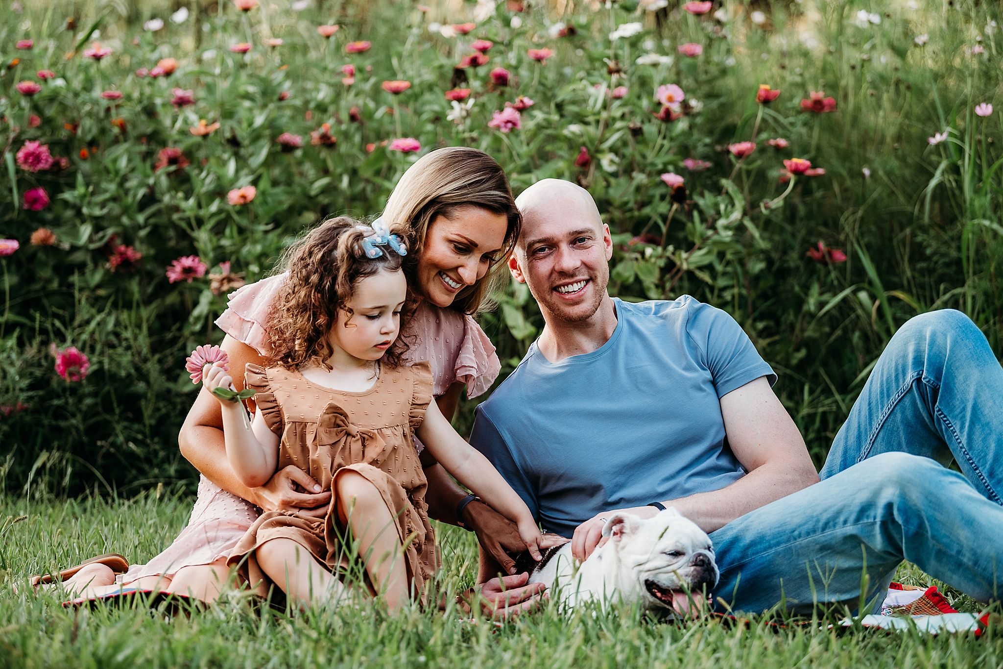 A group relaxes together on grass near blooming pink flowers on a sunny summer day.