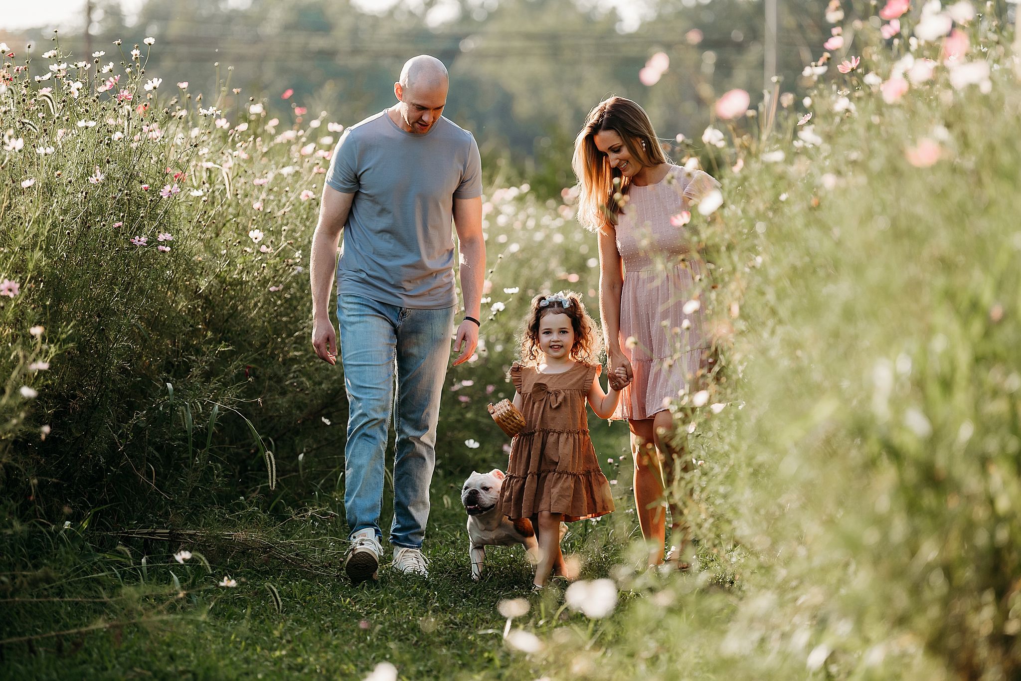 A family walks together through a sunlit meadow filled with delicate wildflowers on a warm summer evening.