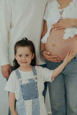 Series of maternity photos with toddler in denim overalls standing next a pregnant belly.