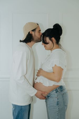 A series of intimate maternity photos showing a couple in white tops and jeans against a light background.