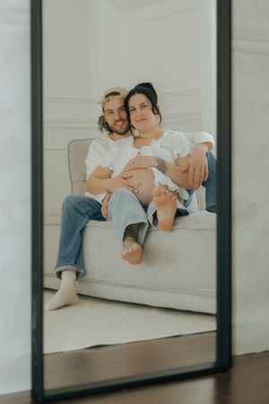 A couple sits together on a white couch, their reflection visible in glass panels.
