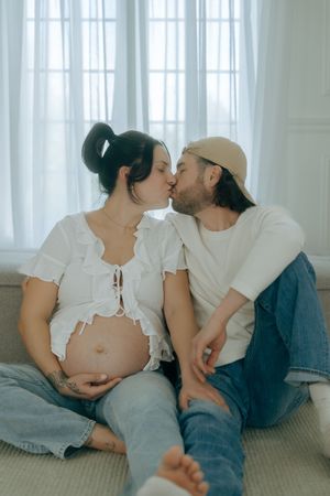 A series of intimate maternity photos showing a couple lying together on the floor near white curtained windows.
