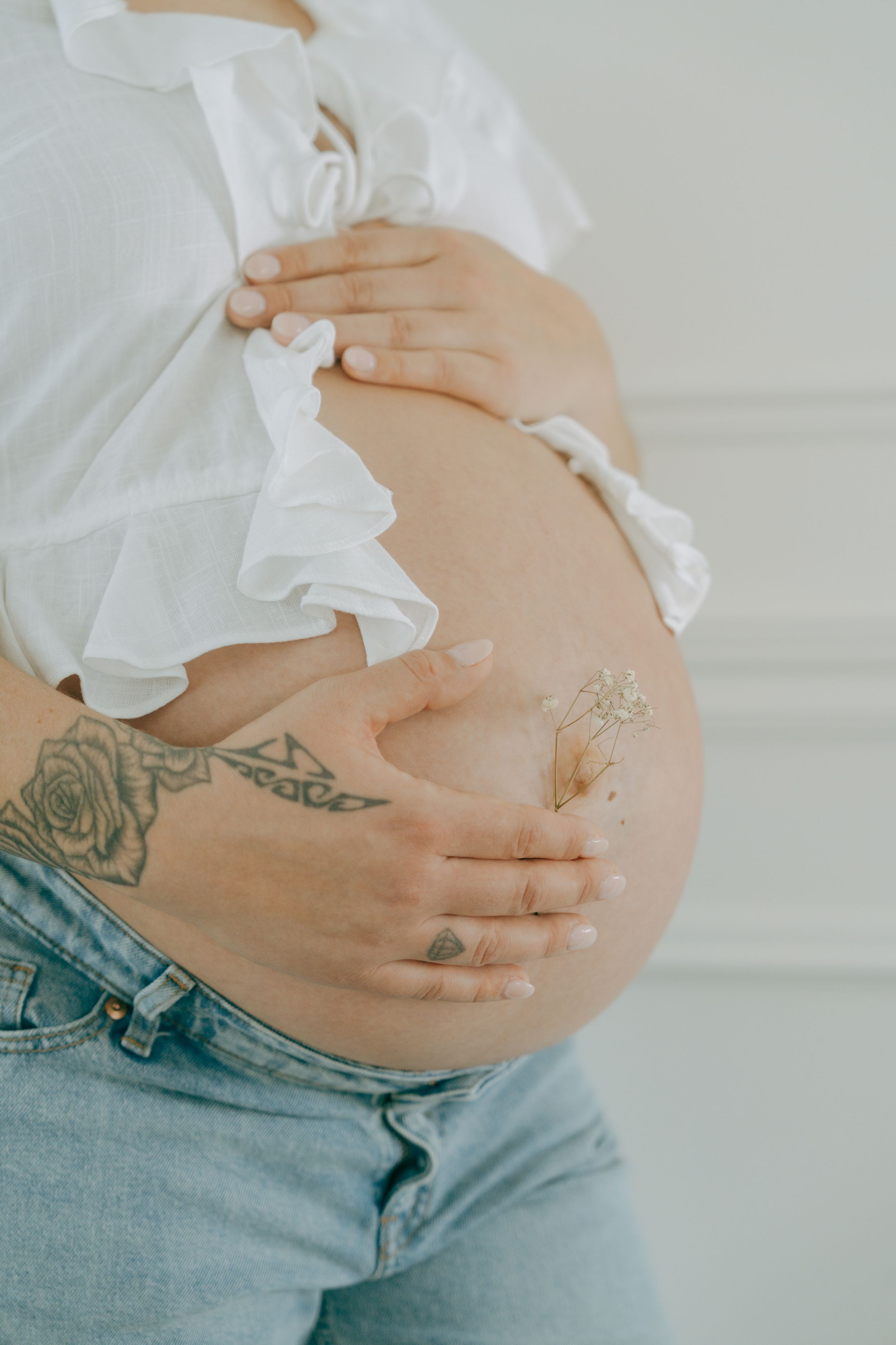 Four images showing a pregnant belly with hands lovingly touching and lotion being applied, wearing blue denim jeans.