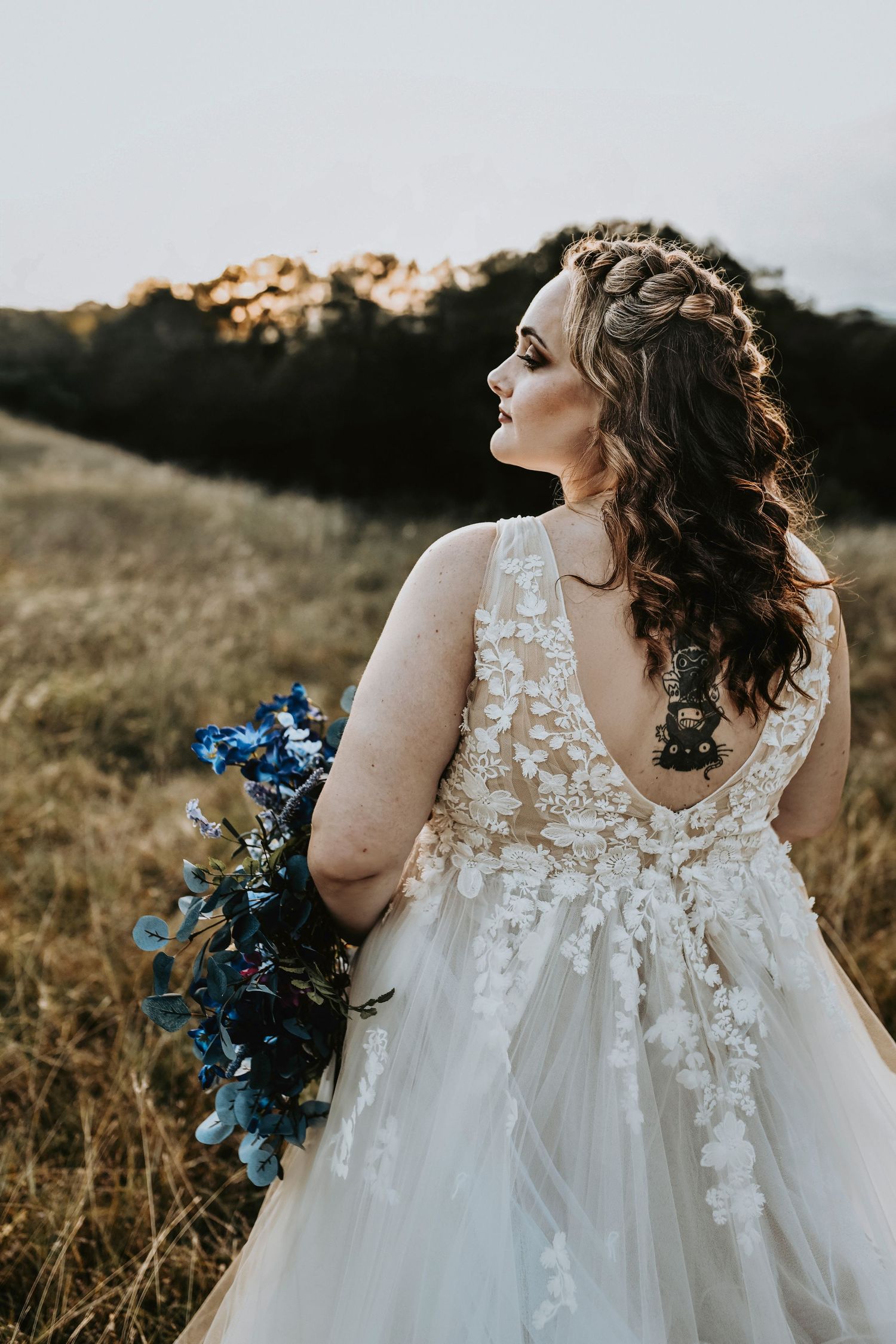 Blonde bride with blue and white vintage heels standing in grassy Texas hills during sunset bridal session.