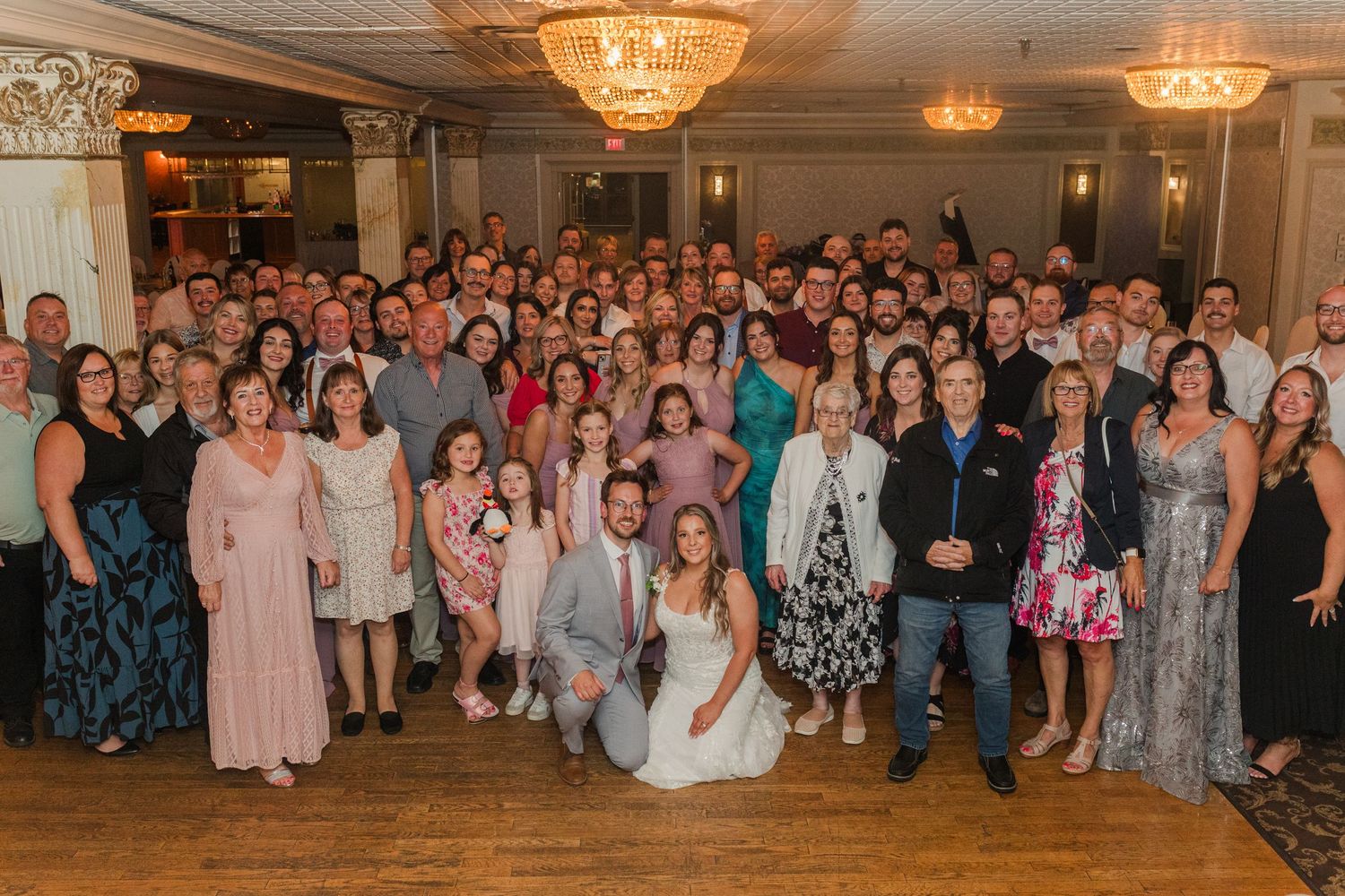 Large celebration in an elegant ballroom with crystal chandeliers and crowd of guests in formal attire.
