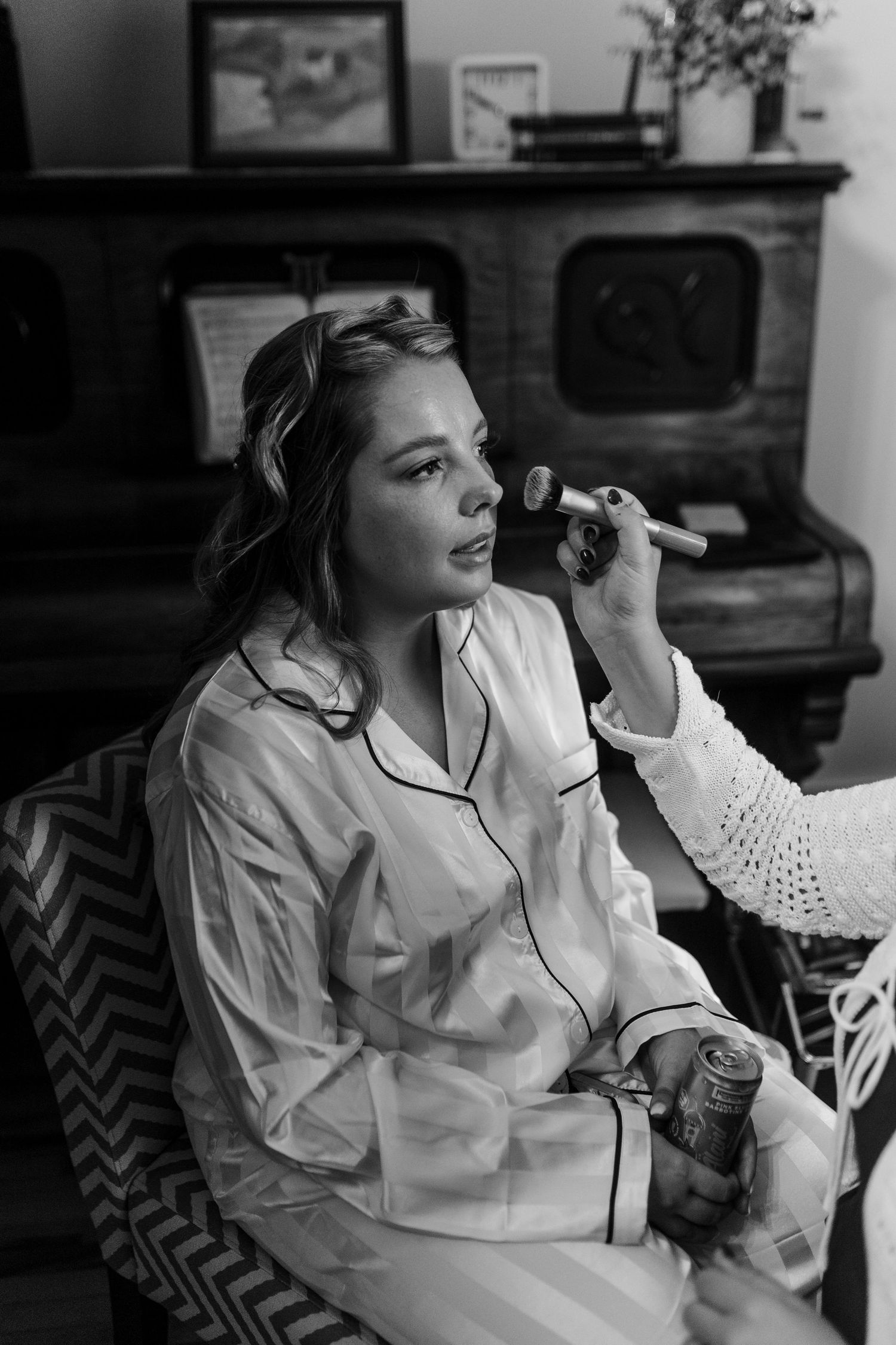 Black and white photo of someone getting makeup applied while wearing a white button-down shirt against a patterned background.