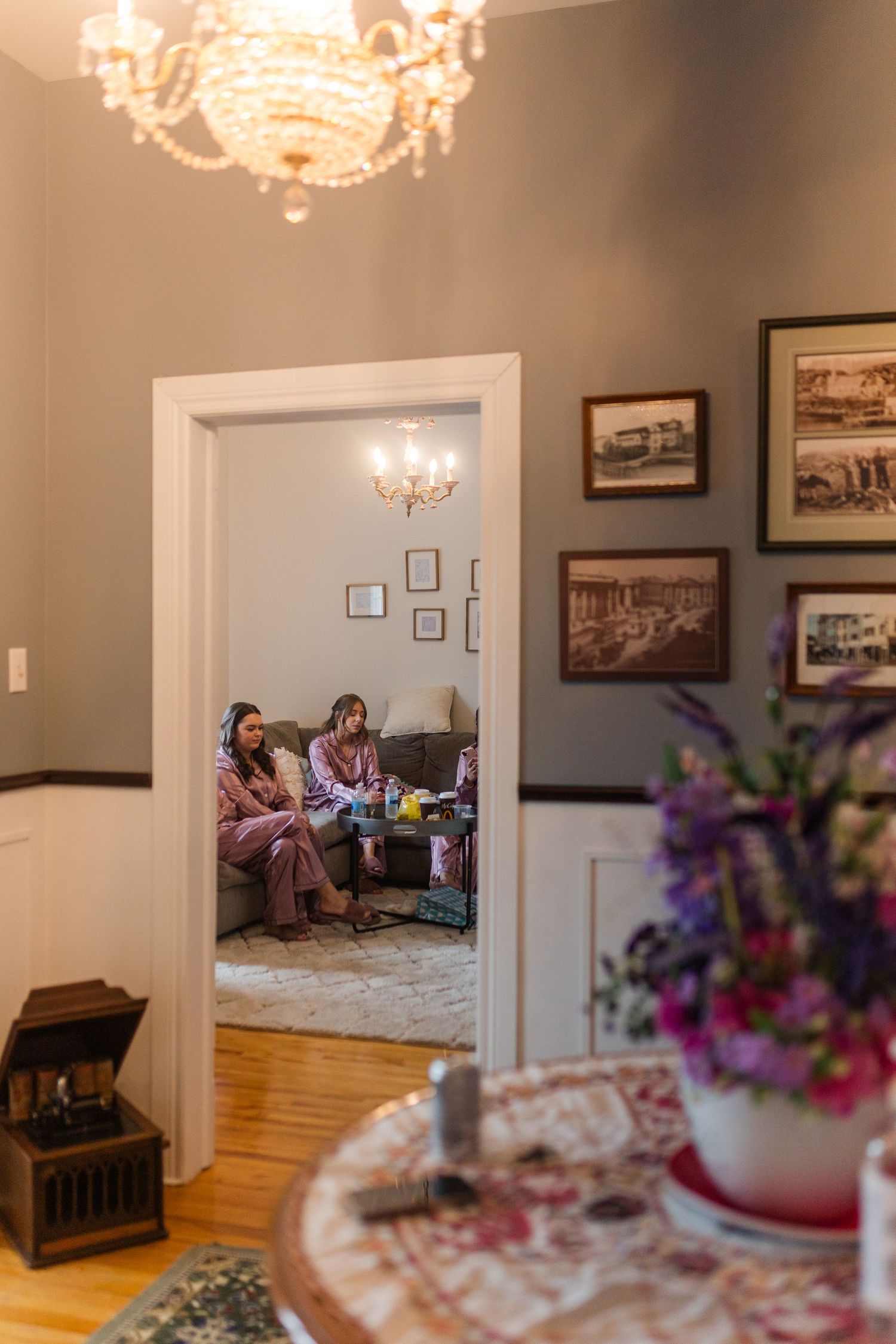 Interior room with vintage decor featuring crystal chandeliers, hardwood floors and historic photographs on the walls.