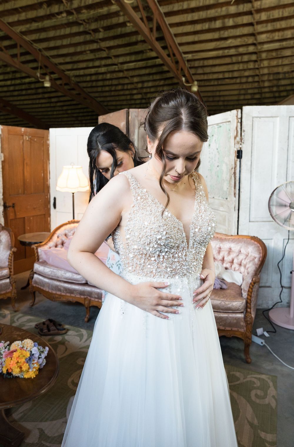 Mother and daughter share emotional embrace in rustic barn while wearing elegant white dresses.
