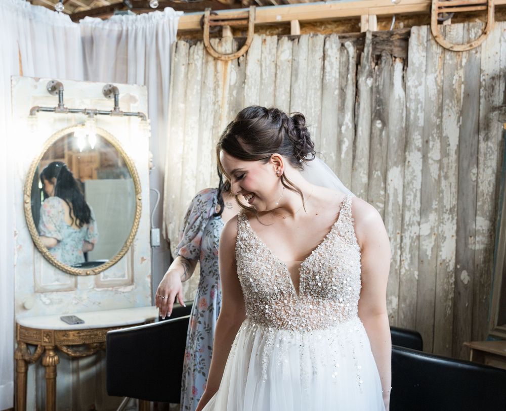 A bridal gown with delicate beaded details and lace accents hangs in rustic barn setting with vintage decor.