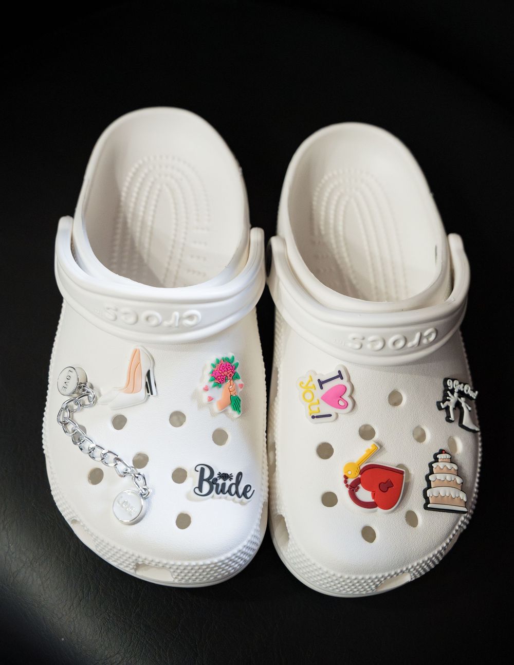 Four white classic Crocs shoes decorated with various charms and pins including butterflies, apples, and cute doodles.