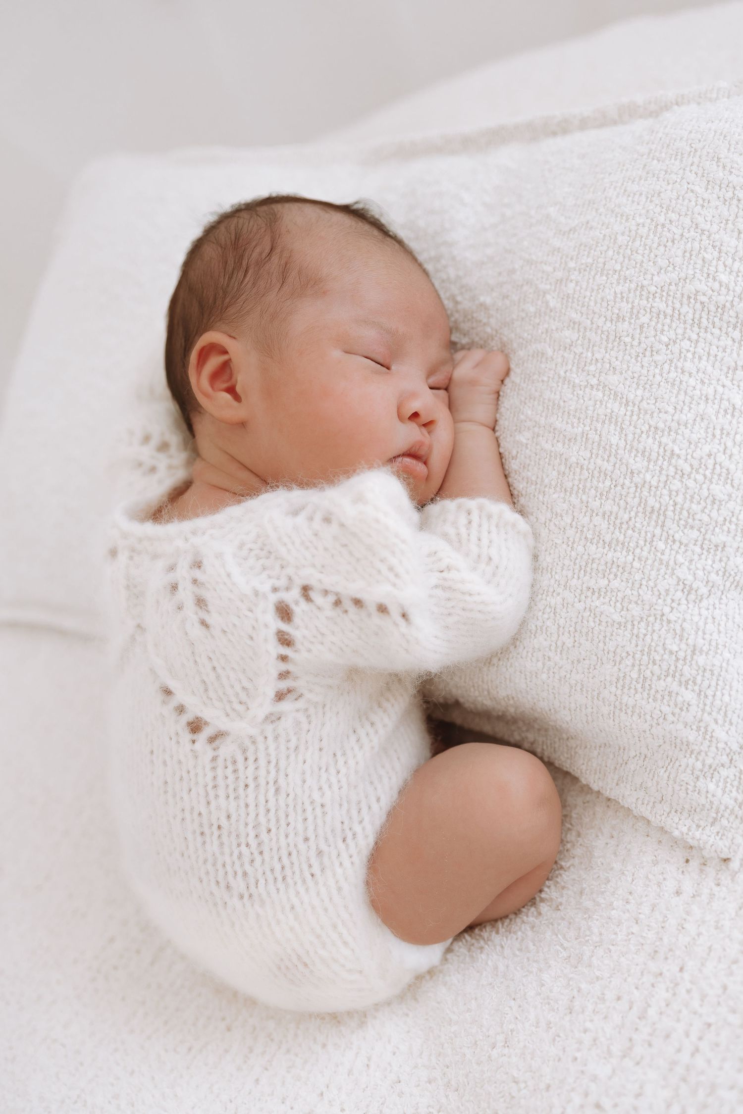 Peaceful newborn baby sleeping on white blanket wearing cozy knit sweater.
