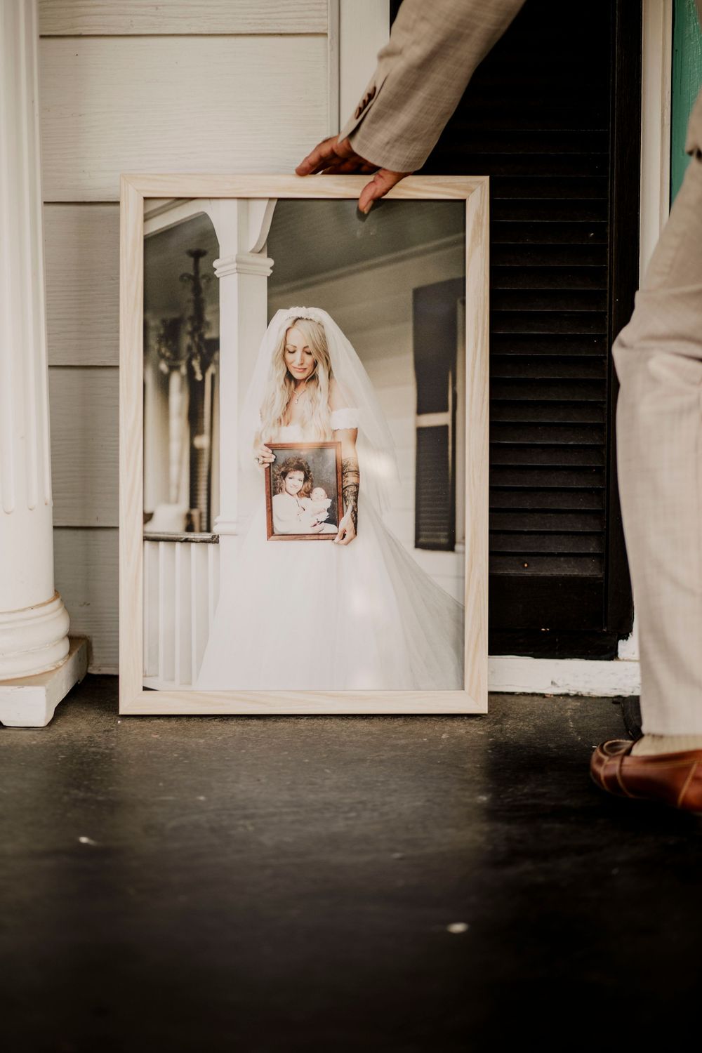 Person holding wedding portrait on a white porch.