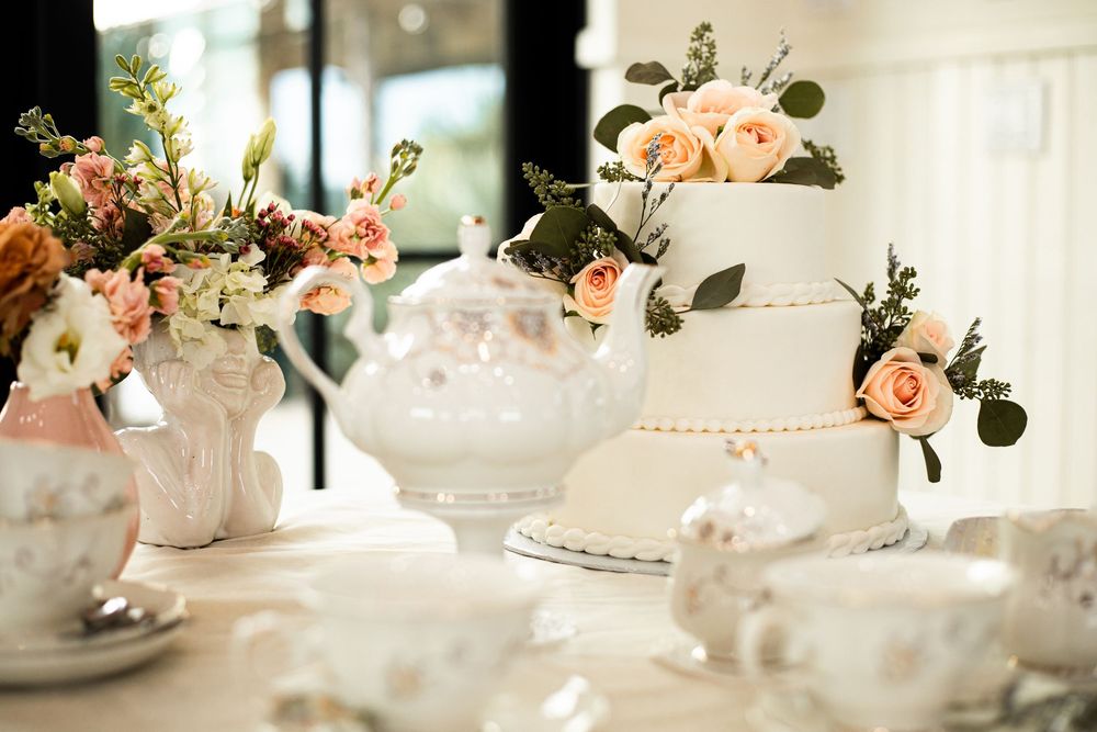 Elegant white wedding cake with peach flowers and teacups on display table.