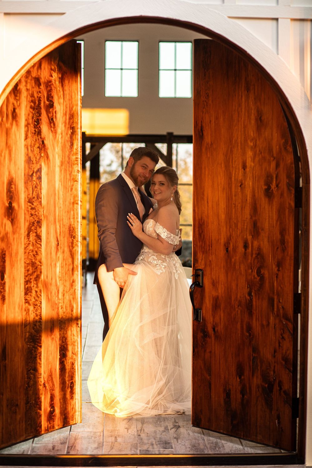 A romantic wedding photo of a couple framed in an arched wooden doorway with warm lighting.