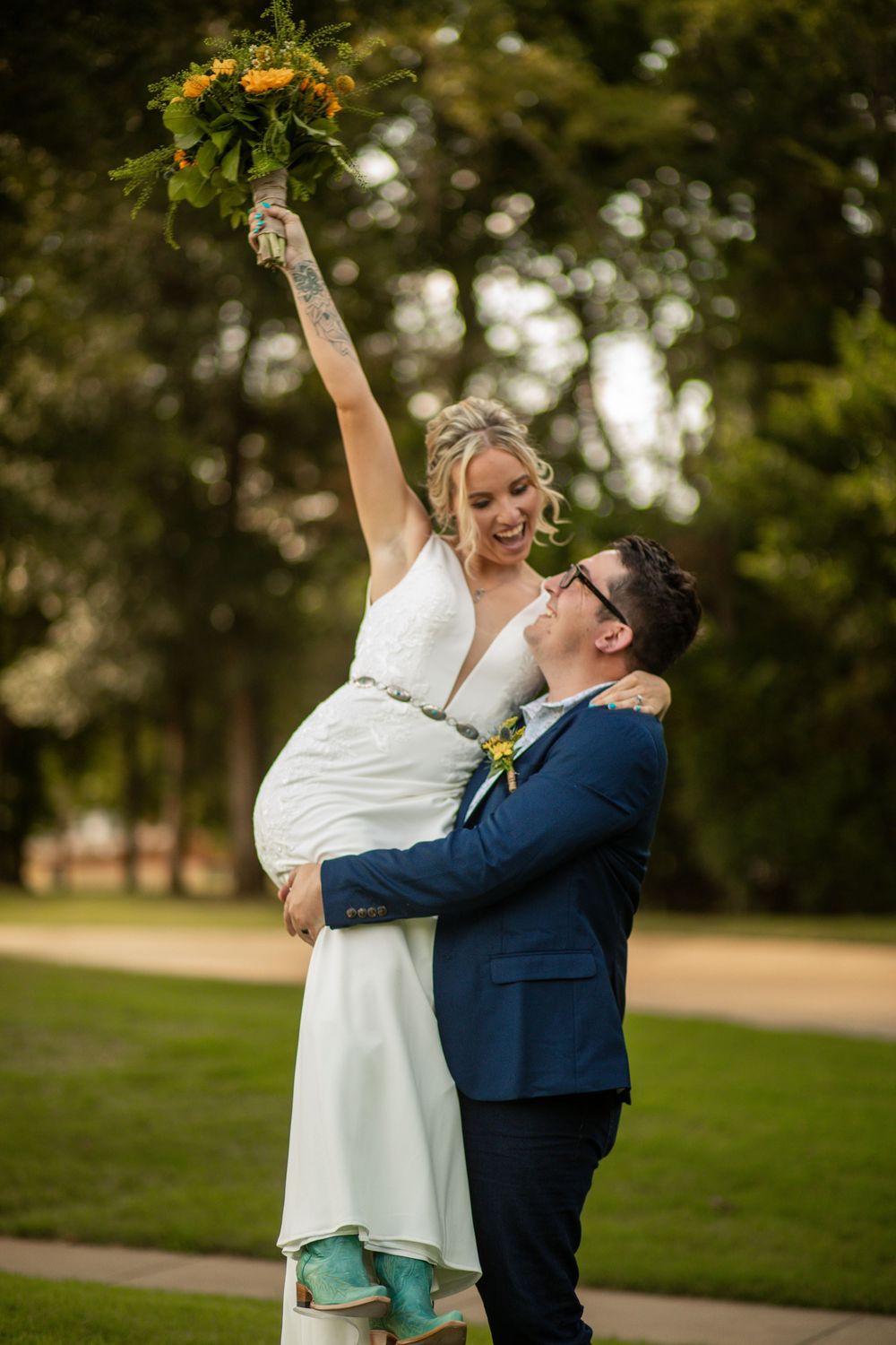 A playful wedding couple dances in a park wearing blue and white attire during golden hour.
