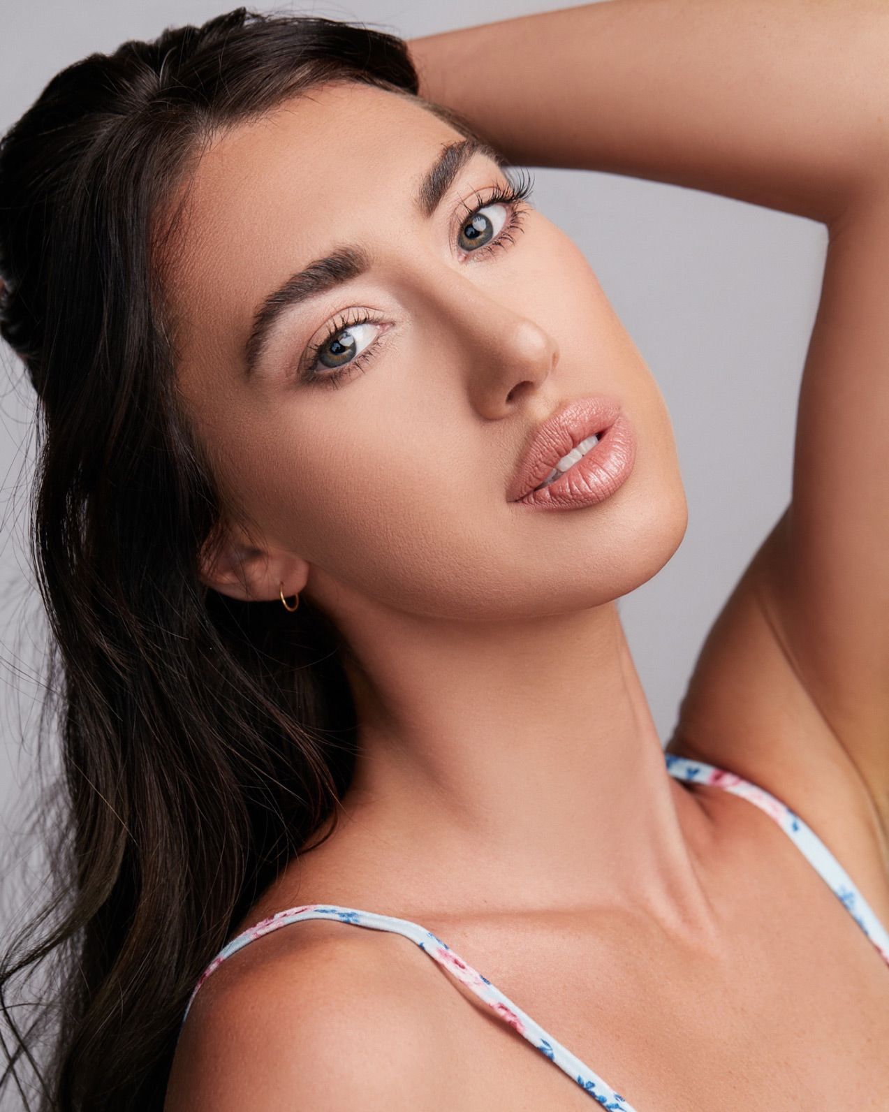 Close up beauty portrait with dramatic lighting showing flawless makeup and long dark hair against light background.