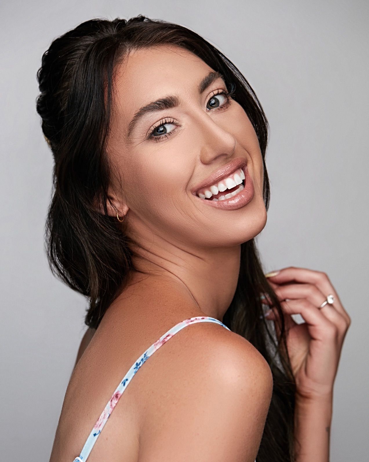 Close up beauty portrait with dramatic lighting showing flawless makeup and long dark hair against light background.