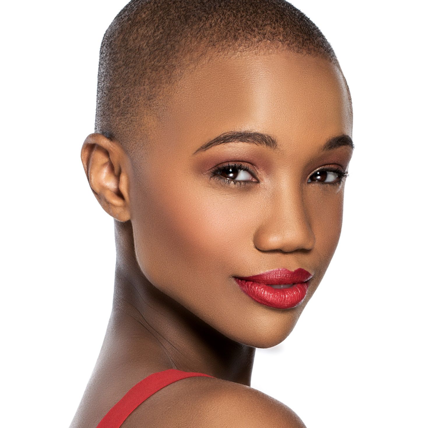 Beauty portrait showing flawless glowing skin, short cropped hair, red lips and makeup against white background.