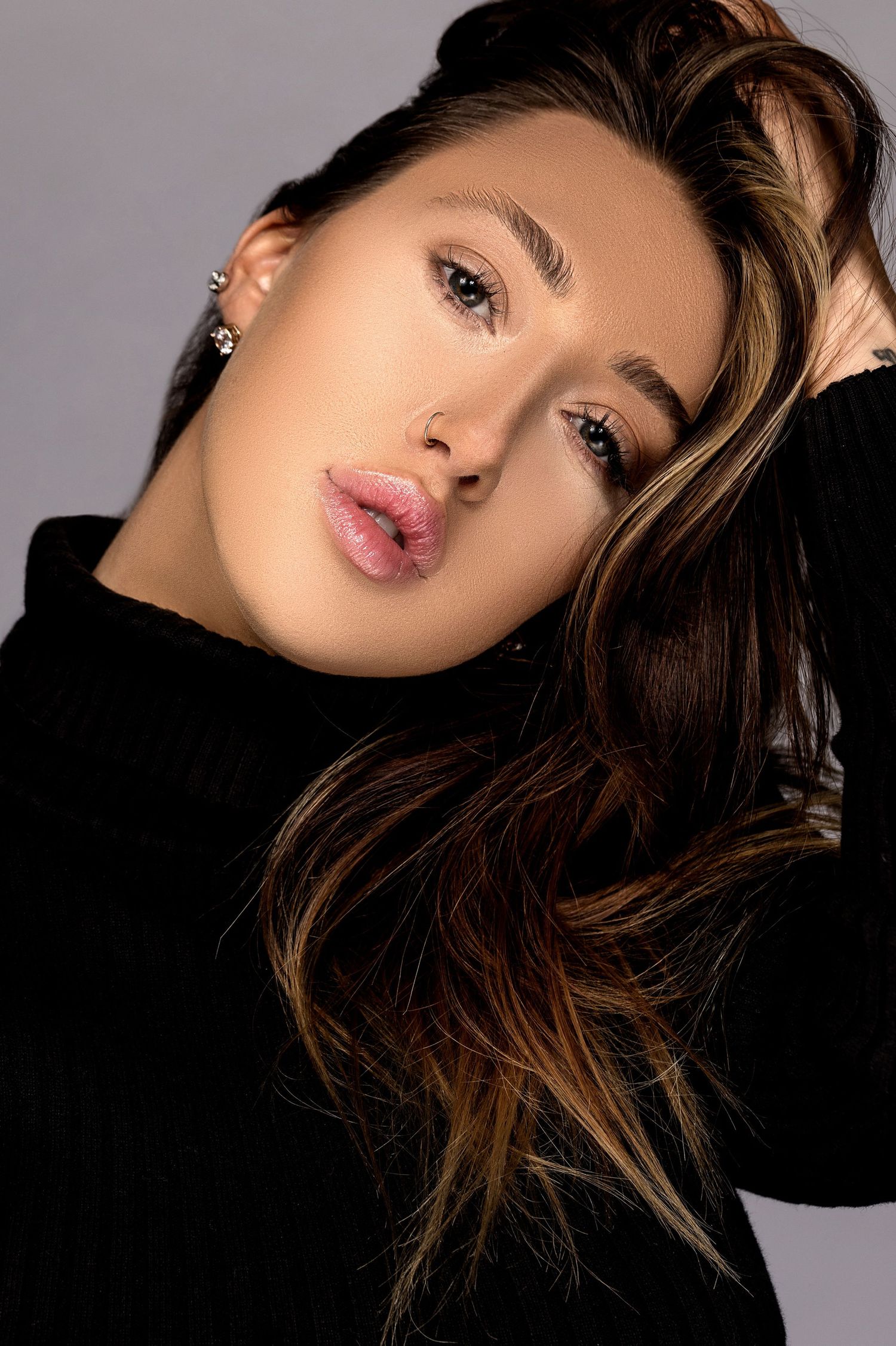 Beauty fashion portrait with dramatic lighting against dark background showcasing wavy brunette hair styling.