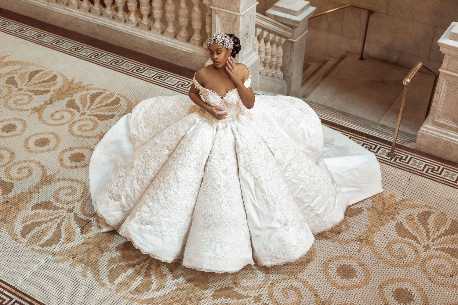 A luxurious white ballgown wedding dress with intricate lace details spreads across an ornate patterned floor.