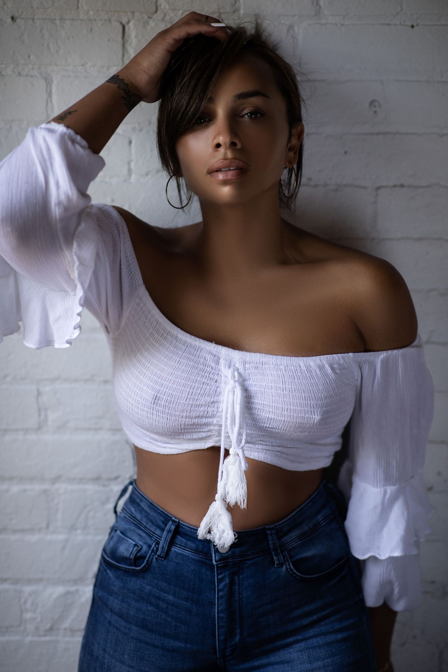 Fashion portrait against white brick wall featuring off-shoulder white crop top and high-waisted jeans.