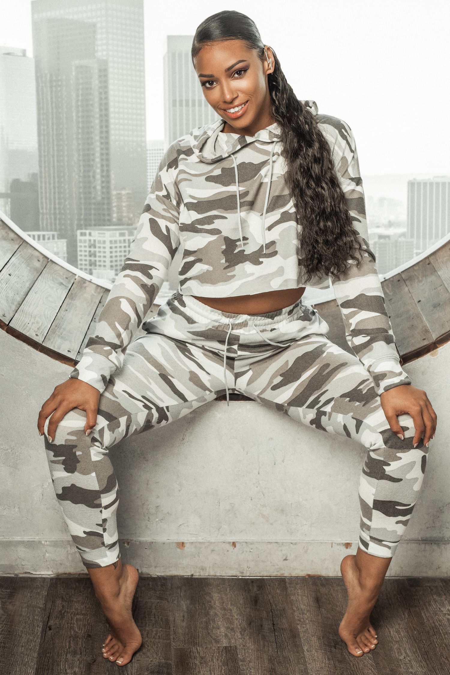 A person sits wearing a trendy gray and white camo print cropped hoodie and matching sweatpants loungewear set.