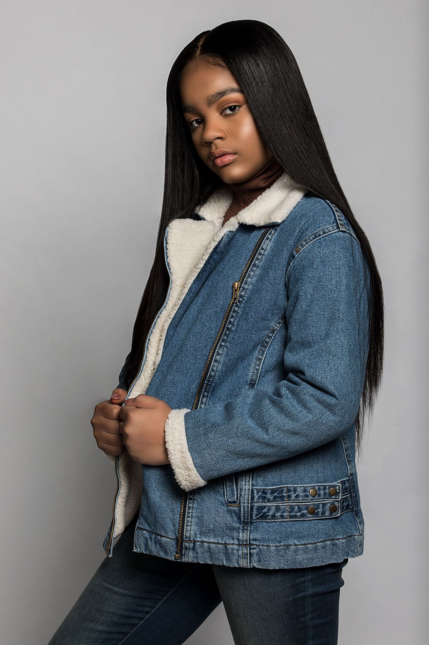 Model posing in cozy sherpa-lined denim jacket and jeans against gray background for fashion photography.