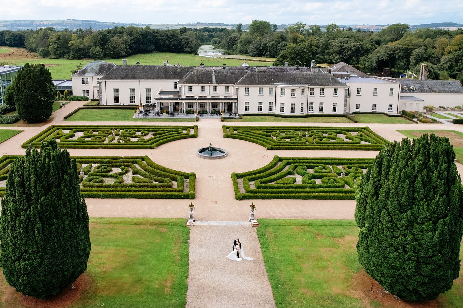 Aerial view of a historic manor house with symmetrical formal gardens featuring manicured hedges and ornate pathways.
