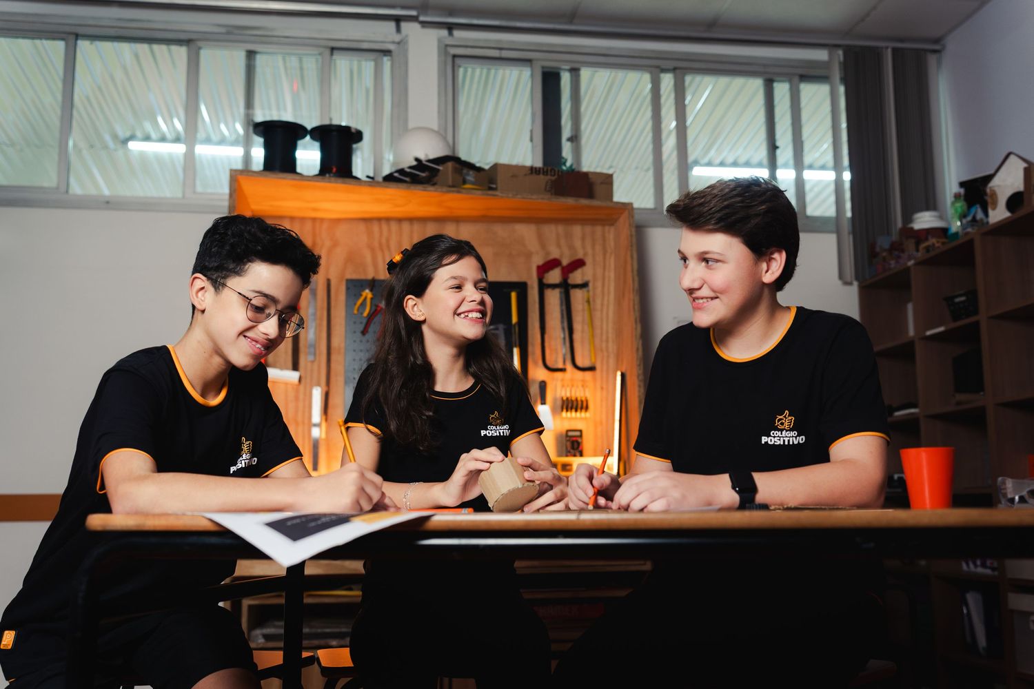 Alunos colaborando em um projeto sentados à mesa em uma sala de aula.