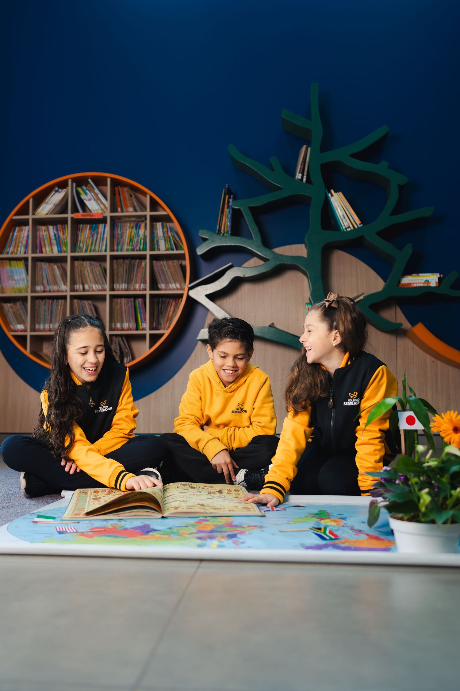 Alunos estudando juntos em um espaço de aprendizagem criativo com estantes exclusivas em formato de árvore. Campanha para escola.