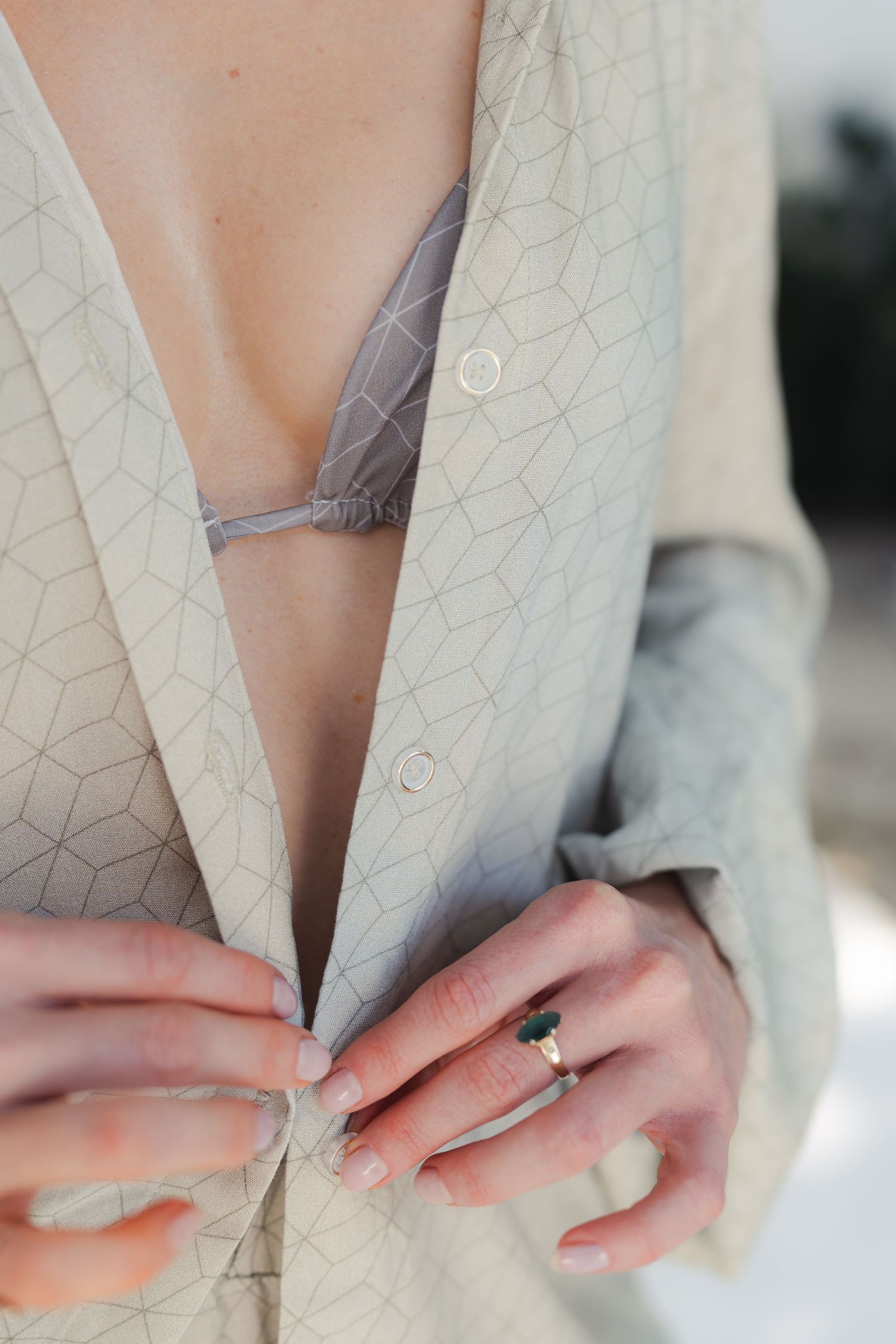 Close-up detail of hands buttoning a light gray geometric patterned shirt.