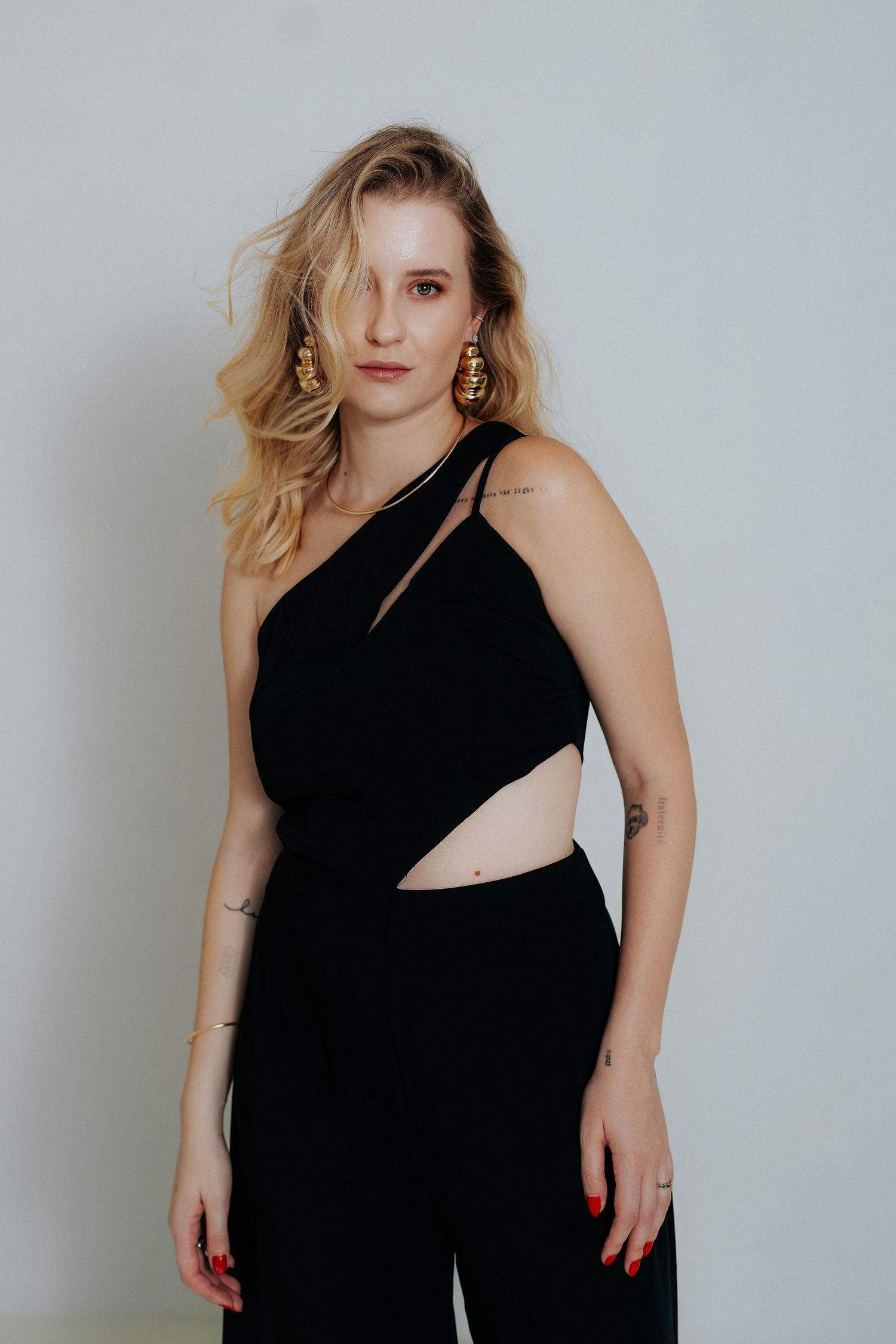 Woman in black sleeveless dress poses against light gray background in fashion photo series.