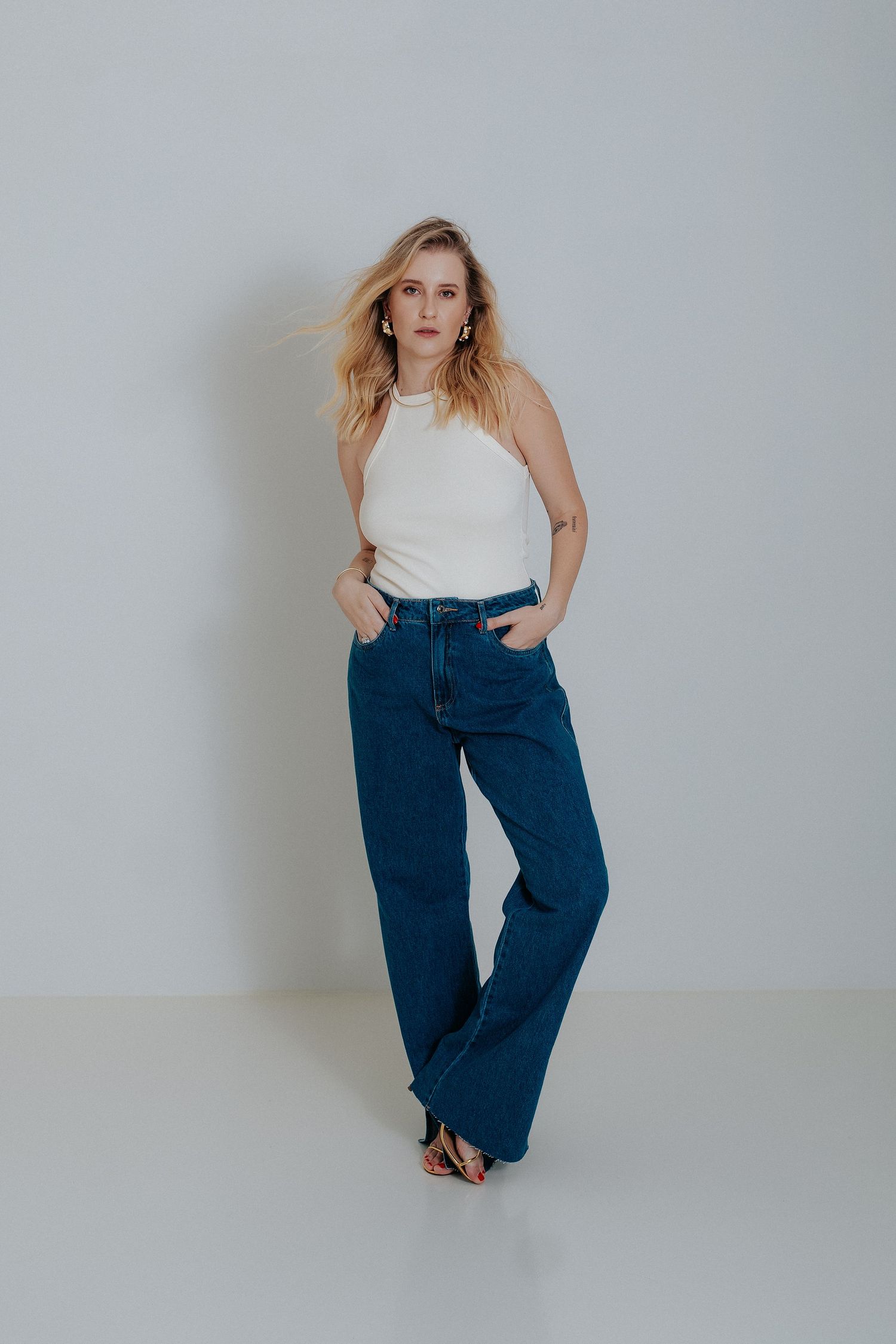 Model in white top and baggy blue jeans poses against white wall in casual fashion photoshoot series.