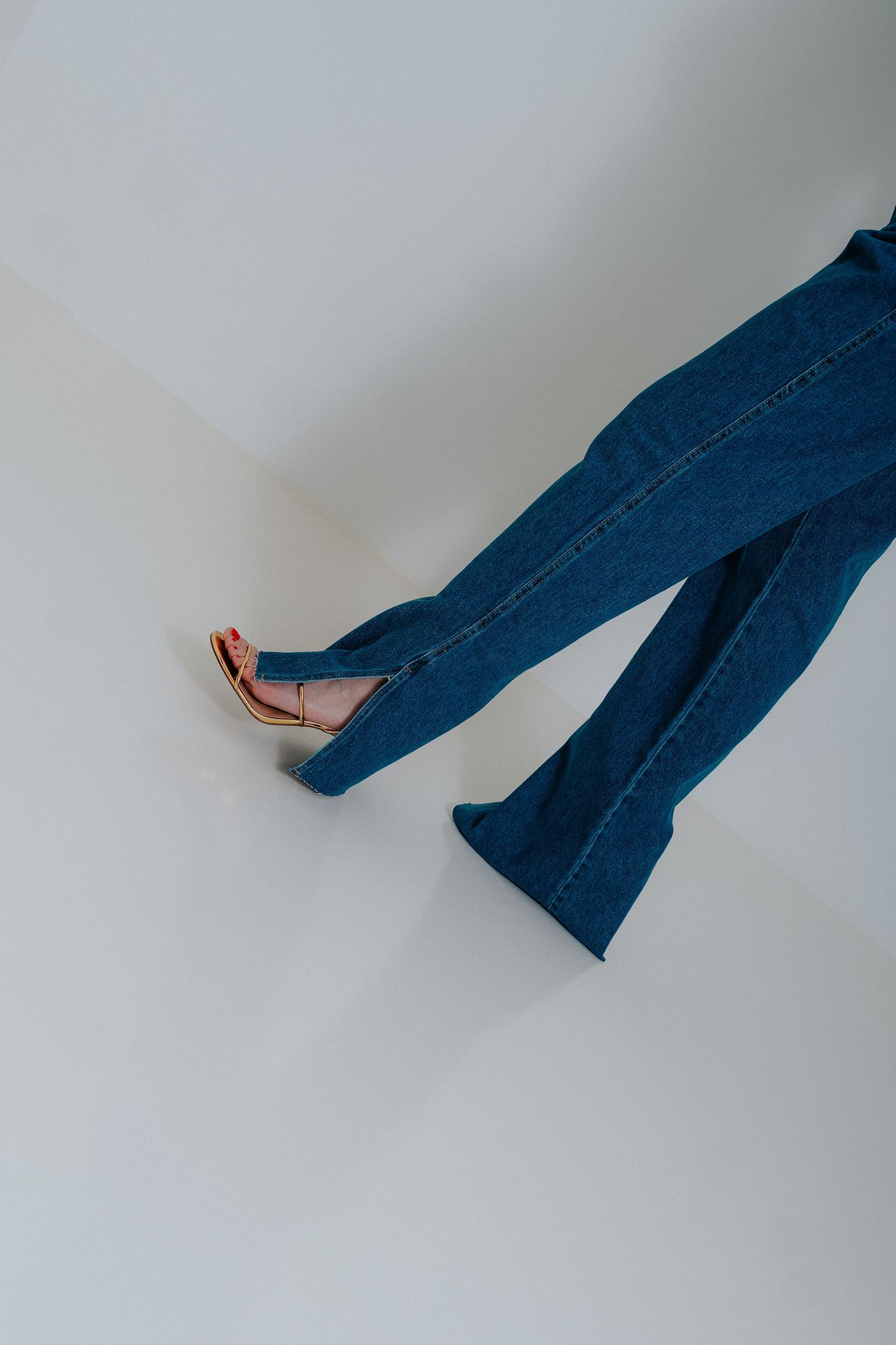 Legs wearing flared blue jeans and red high heel shoes against a white background.