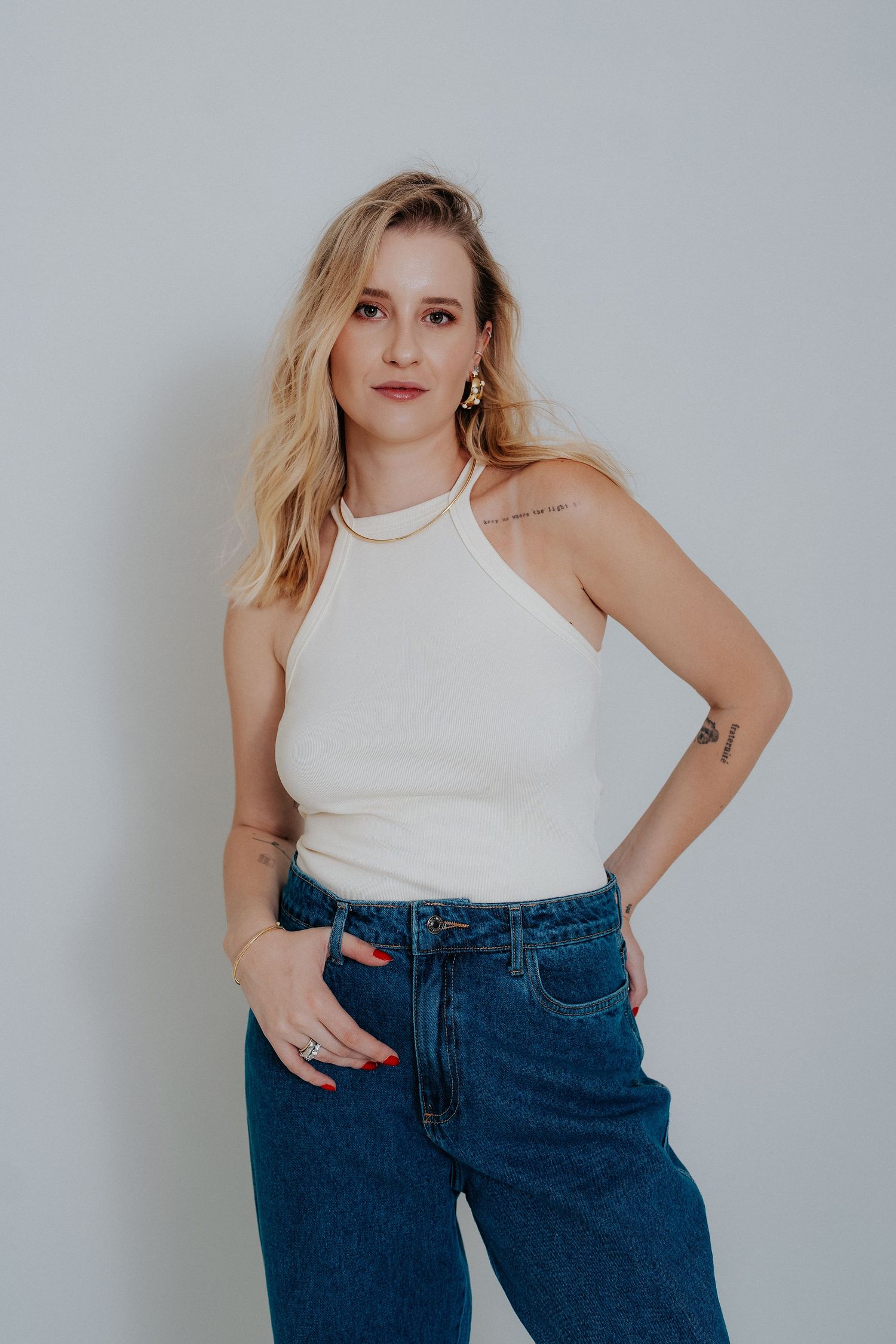 A person in a white sleeveless top and blue jeans poses against a light gray background in a series of photos.