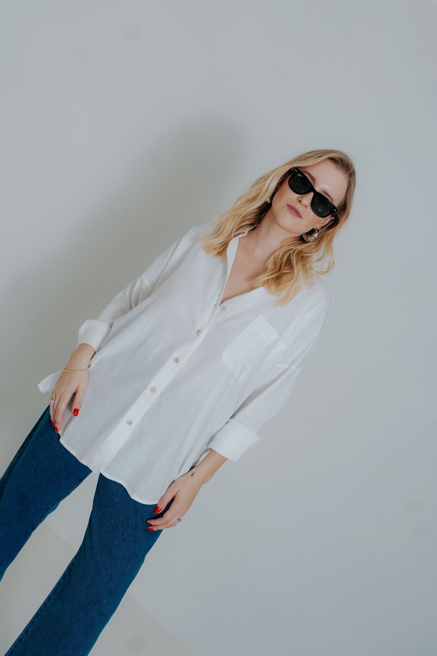 A person in a white button-down shirt and blue jeans poses against a light background in a fashion-forward series.