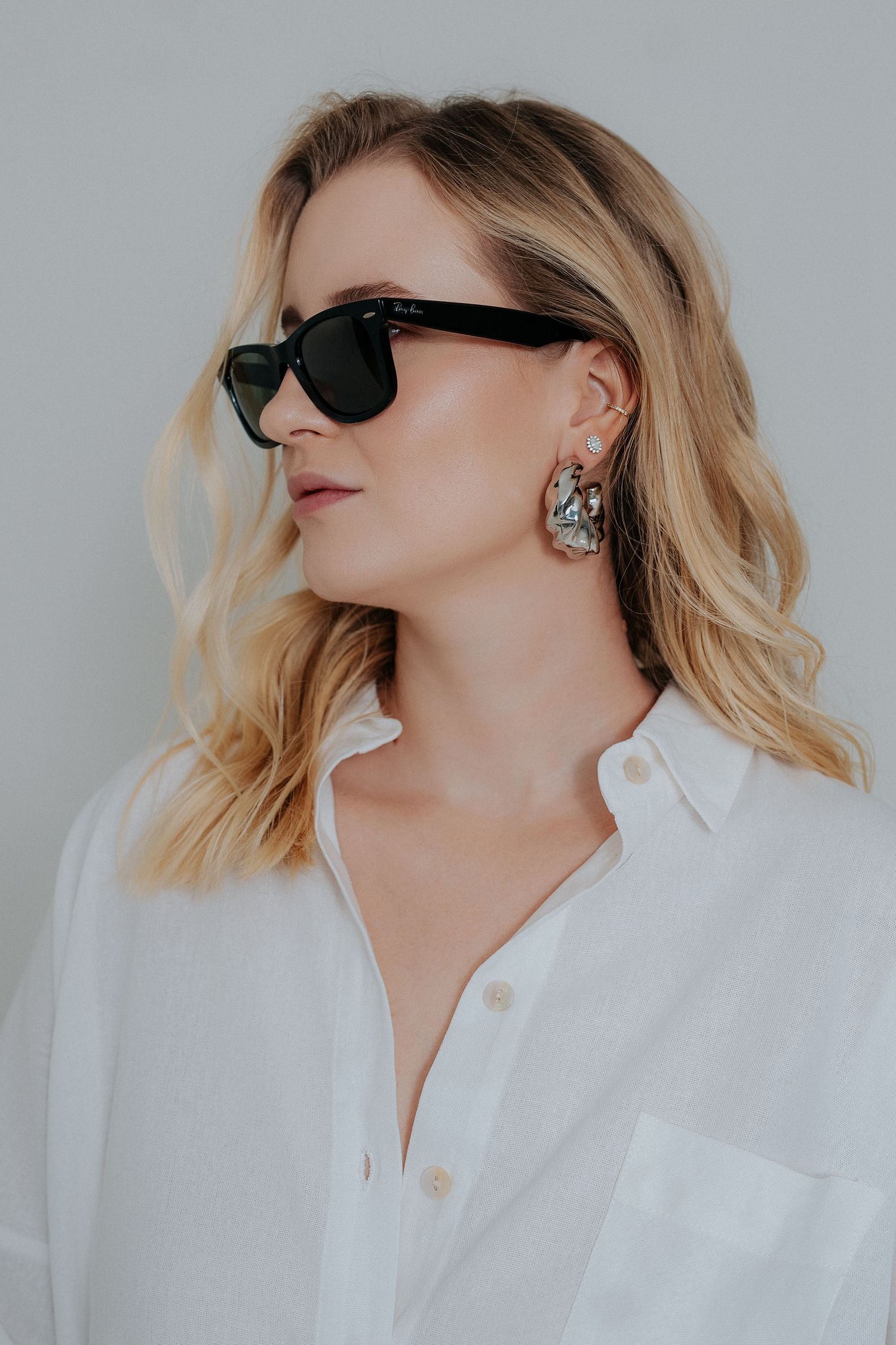 Fashion model in white button-down shirt and black sunglasses poses against light background in editorial style photos.