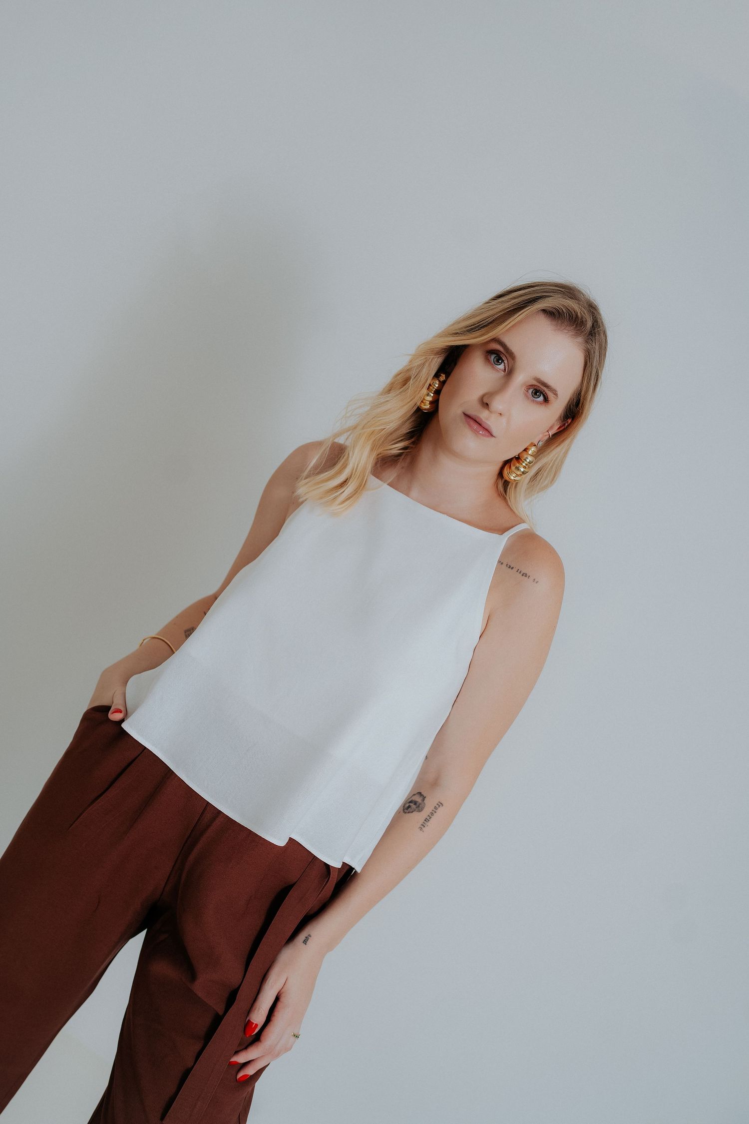 Fashion model poses in white sleeveless top and brown pants against neutral background in minimalist style series.