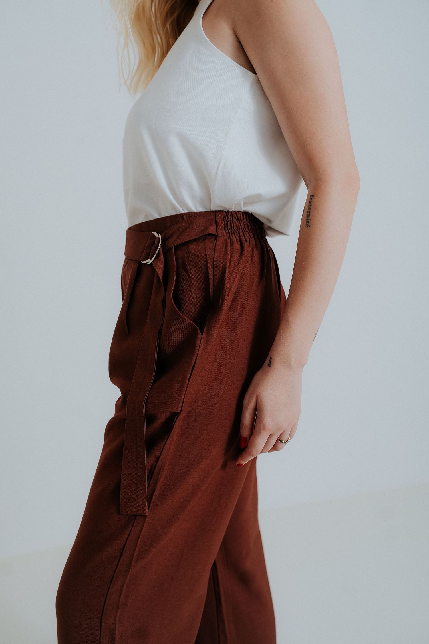 Close-up view of brown linen pants with drawstring waist and pockets against a white background.